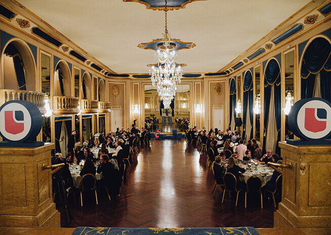 Invitados sentados en una cena de gala en un salón lujoso con candelabros opulentos, exudando una atmósfera clásica y sofisticada.