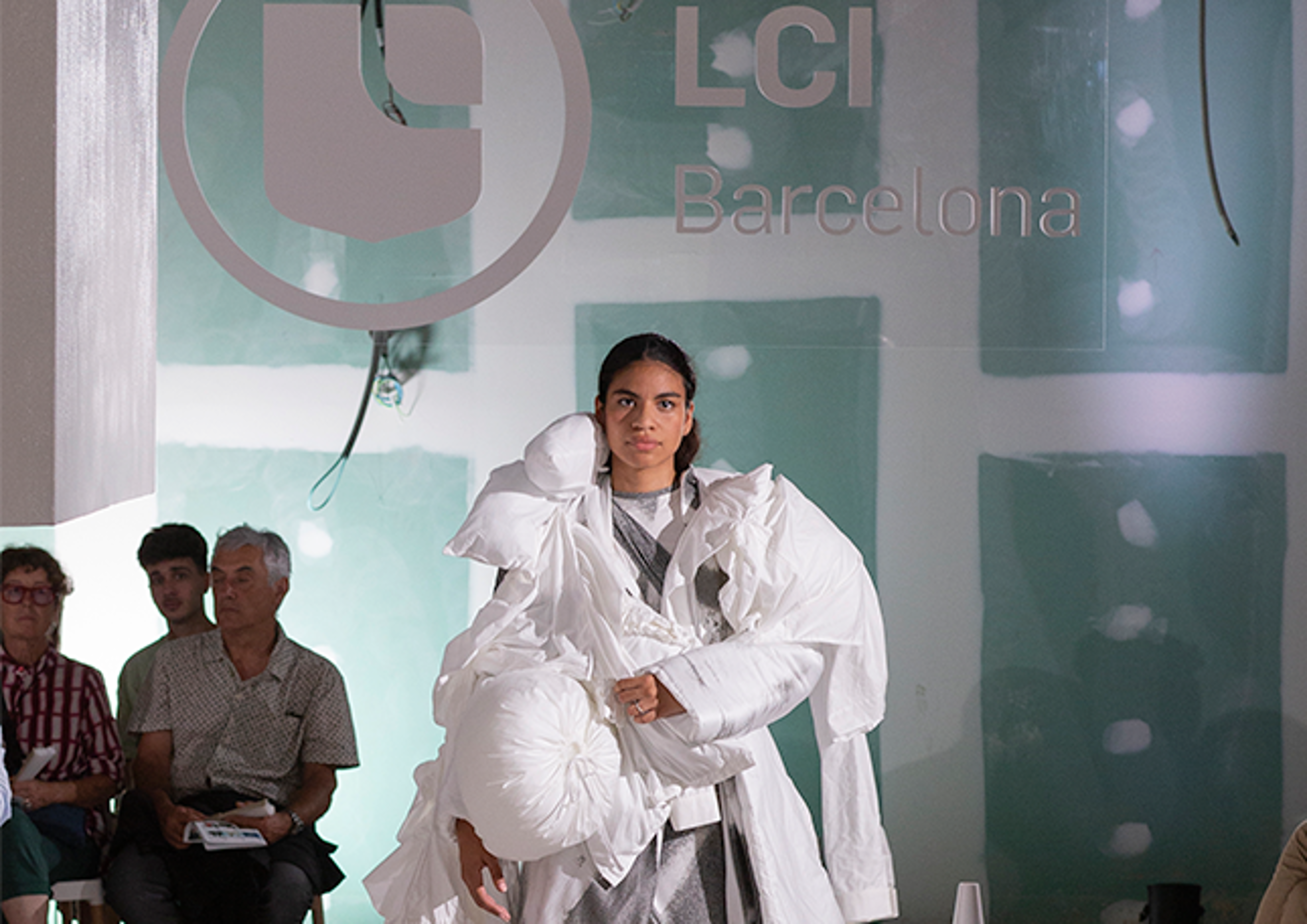 A model confidently showcases an avant-garde white outfit on the runway at LCI Barcelona's fashion event.