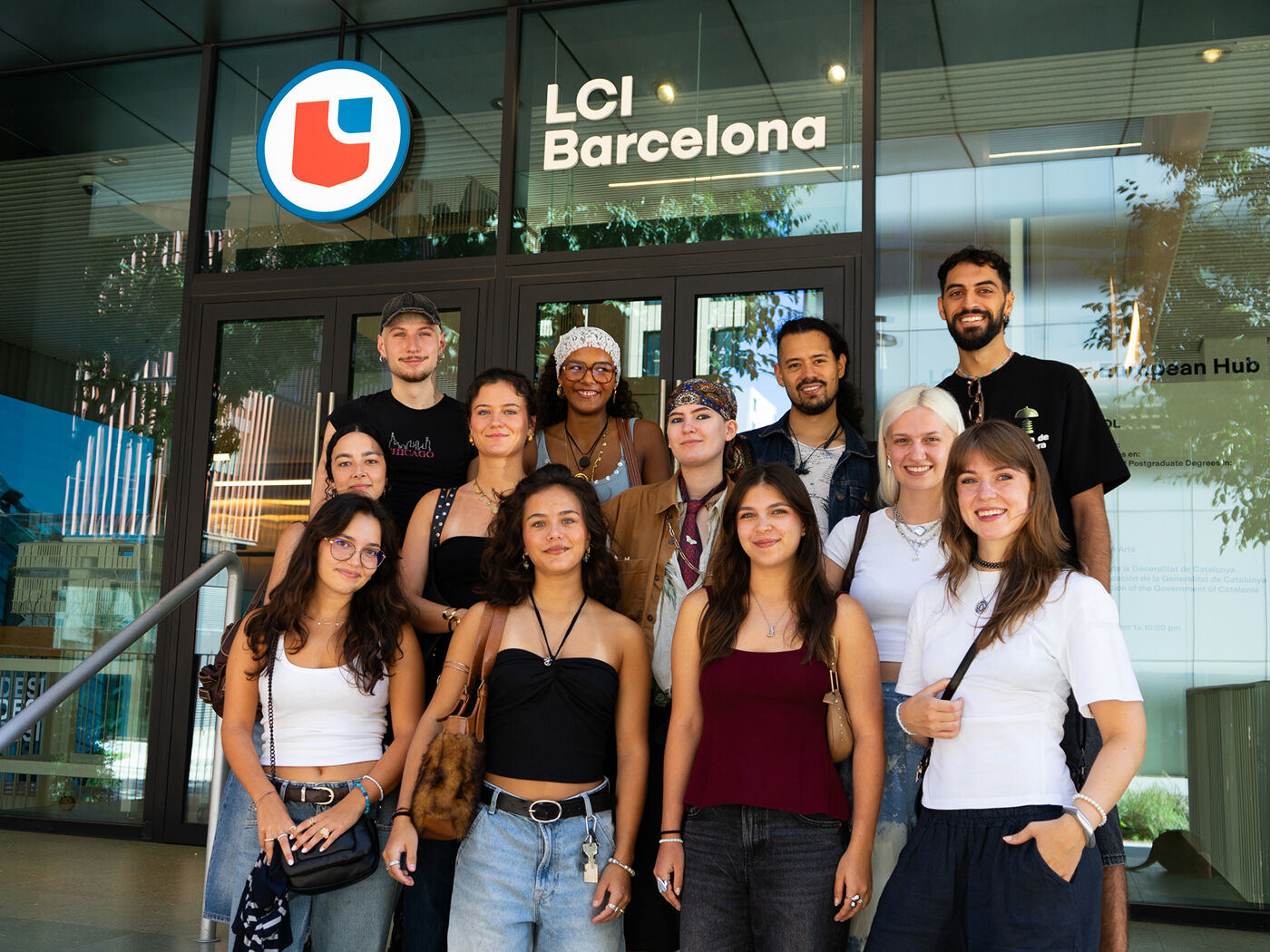 A group of diverse people are standing in front of LCI Barcelona. They are smiling and posing for a photo. The group consists of both men and women of varying ages and ethnicities.
