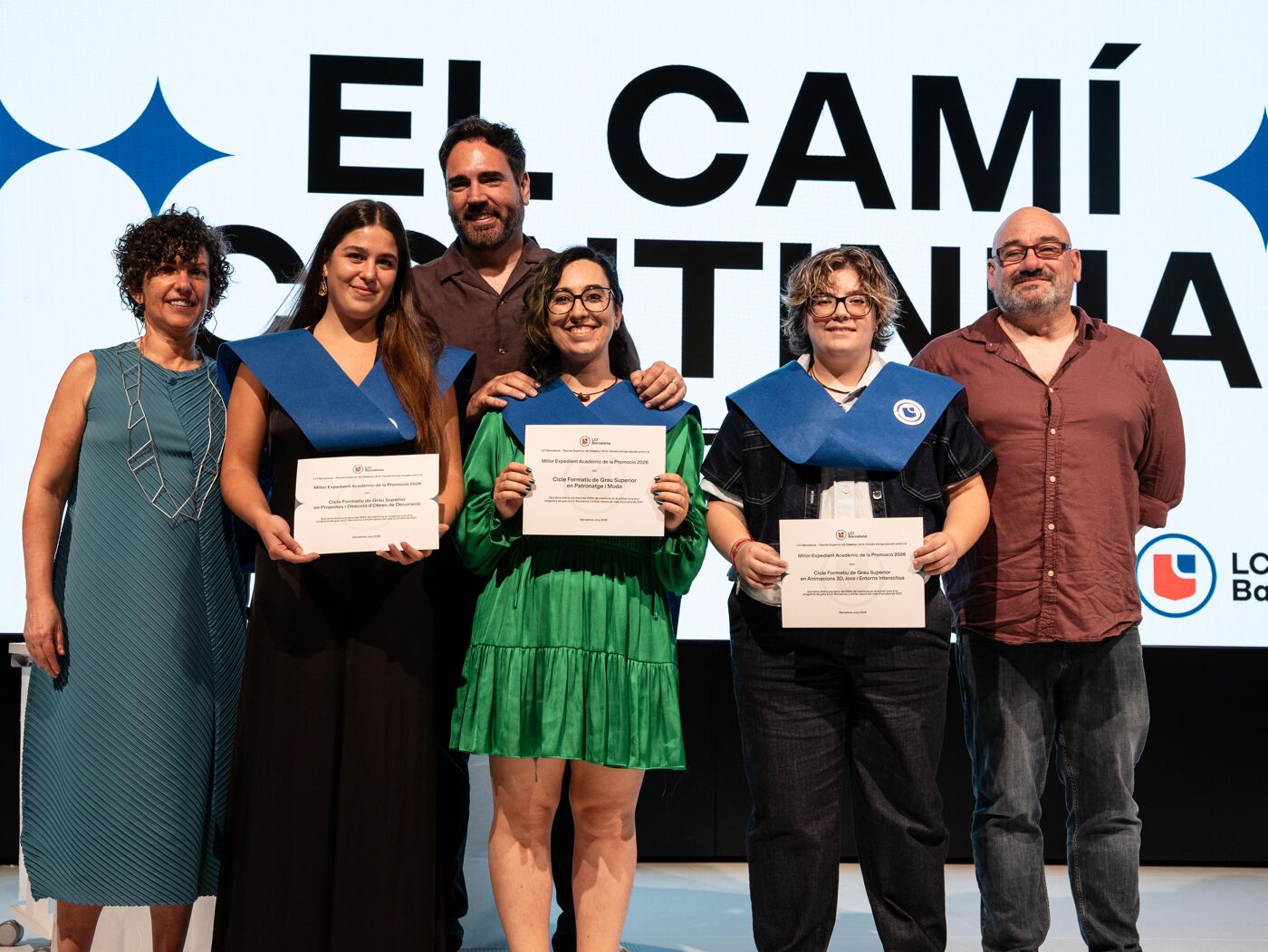 Six people are celebrating an academic achievement, with three women receiving certificates and gowns, while two men and one woman accompany them on a stage with a backdrop reading "THE JOURNEY CONTINUES".
