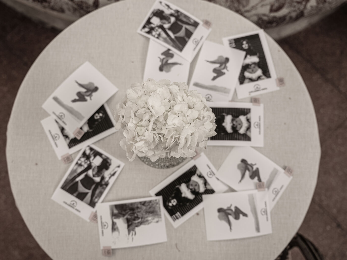 A bouquet of white flowers sits at the center of a table with various cards arranged around it, each featuring a black and white image of a woman in different poses.