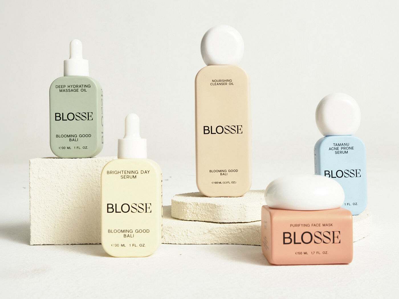 This image showcases five skincare products from the BLOSSE brand, including oils, serums, and a face wash, elegantly displayed on stone blocks.