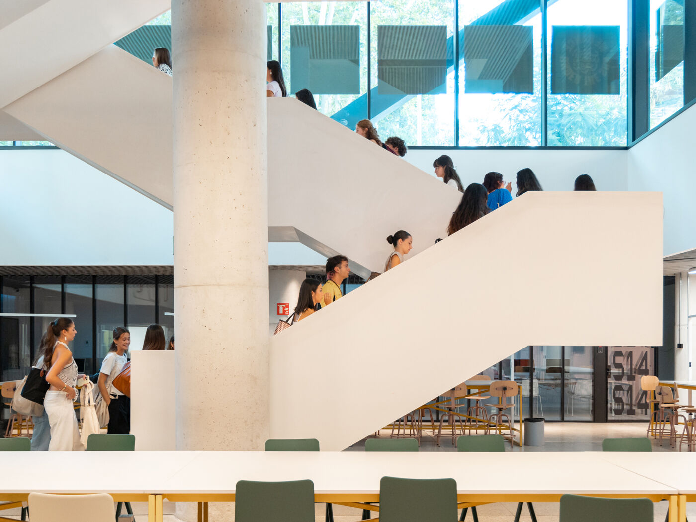 A group of students ascends a large, white staircase inside a modern, sunlit building.