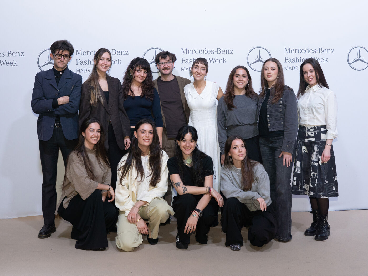 A group of women and two men pose together in front of a white backdrop featuring the Mercedes-Benz Fashion Week Madrid logo.