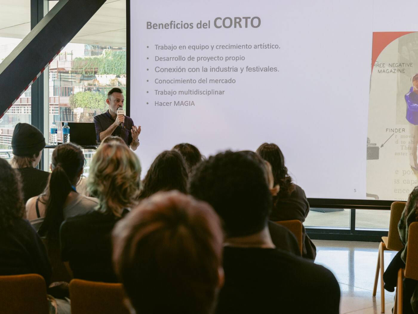 A speaker presents the benefits of making short films to an audience, highlighting teamwork, project development, and market knowledge.