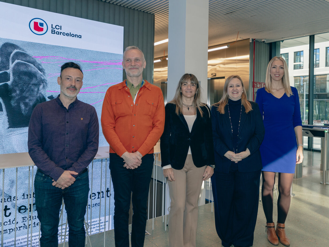 Five people stand in front of a screen that says LCI Barcelona. The men wear shirts, the women wear dresses or jackets.