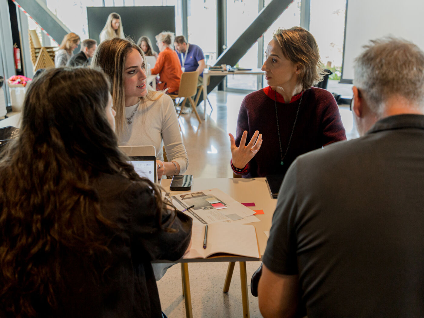 A group of people are seated around a table, engaged in a meeting or discussion. It appears to be a brainstorming session or a team collaboration meeting.