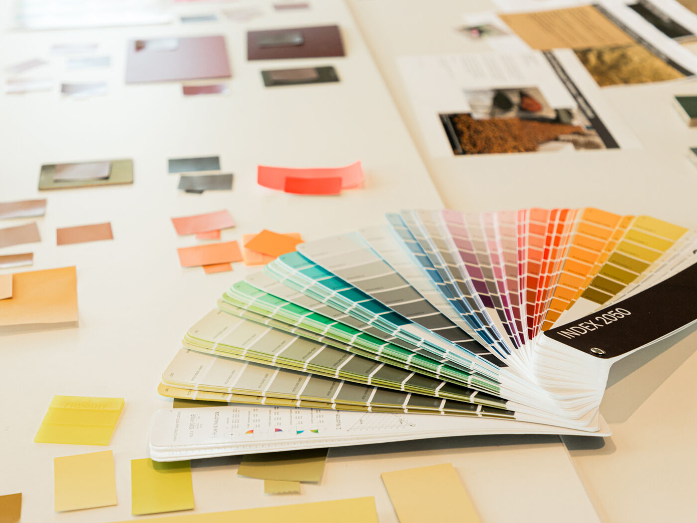 A fan of color swatches is open on a table with various material samples and color cards scattered around.