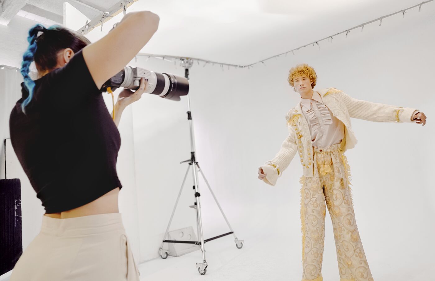 A photographer capturing a fashion model in a dynamic pose during a studio photo shoot.