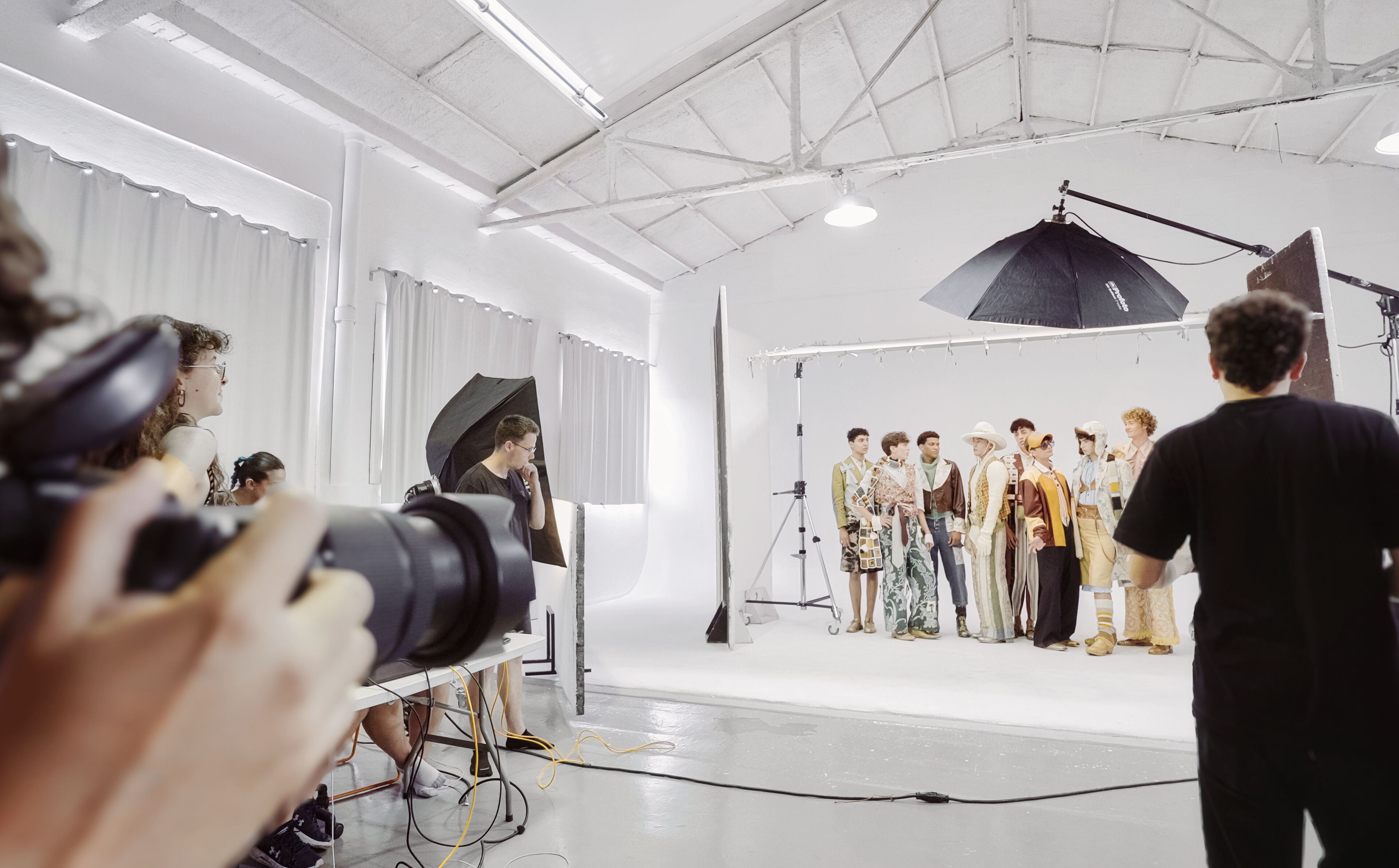 Una mirada entre bastidores a una sesión de fotos de moda con modelos y fotógrafos en un entorno de estudio profesional.