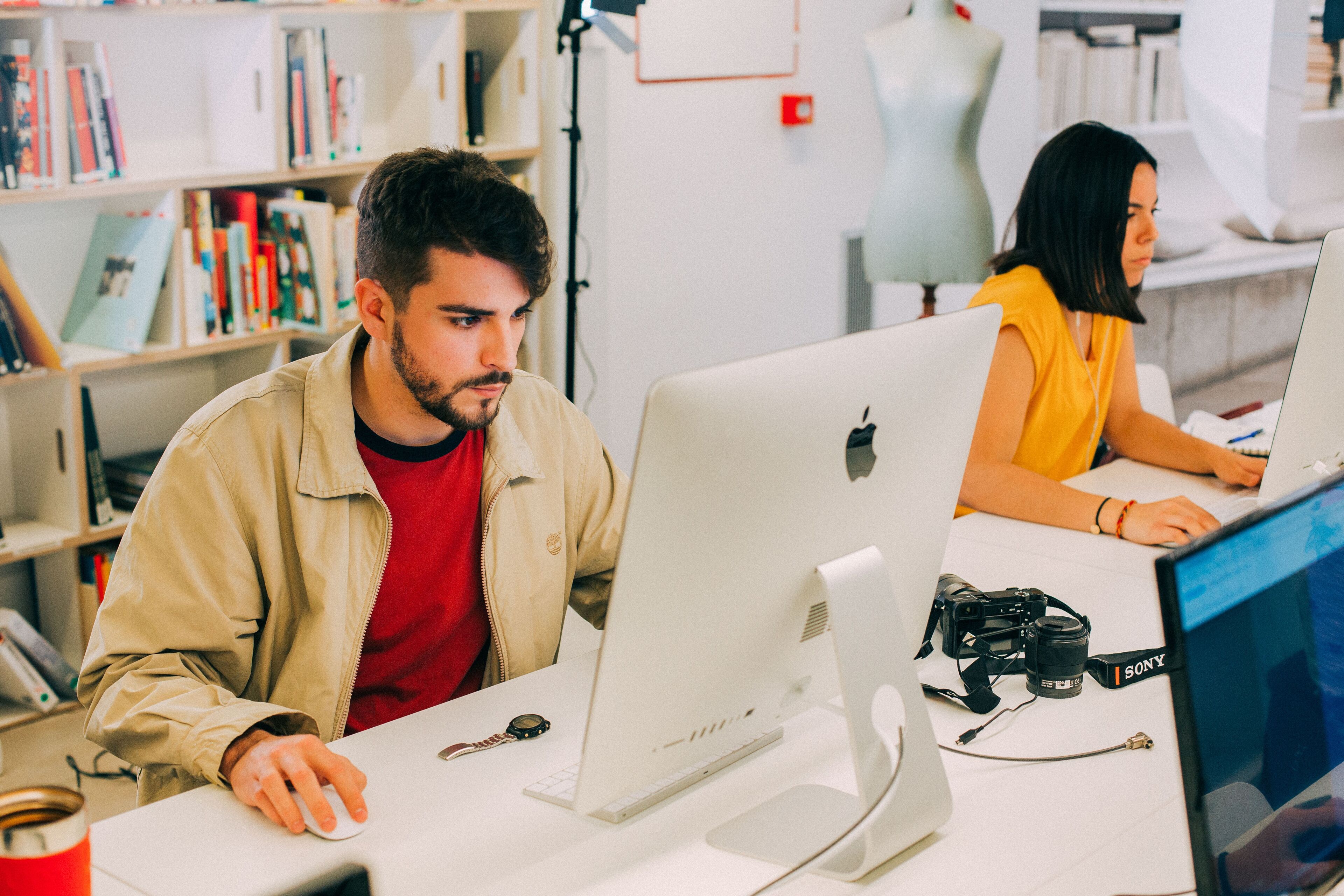 Dos individus concentrats treballen en ordinadors Apple en un entorn d'oficina modern.
