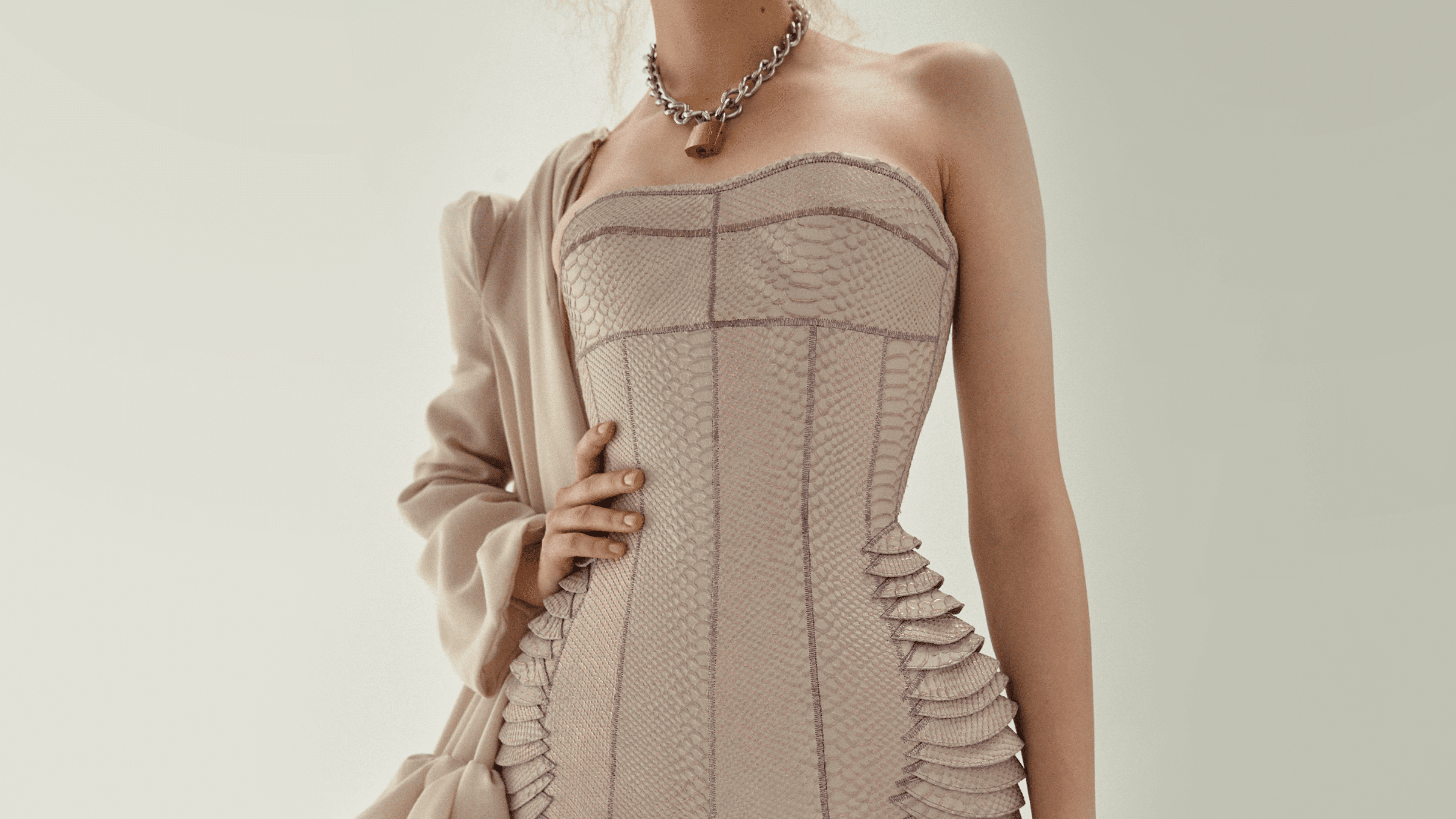 Close-up of a woman in a contemporary corset dress with intricate detailing and a chic overcoat, showcasing a blend of modern and classic fashion.