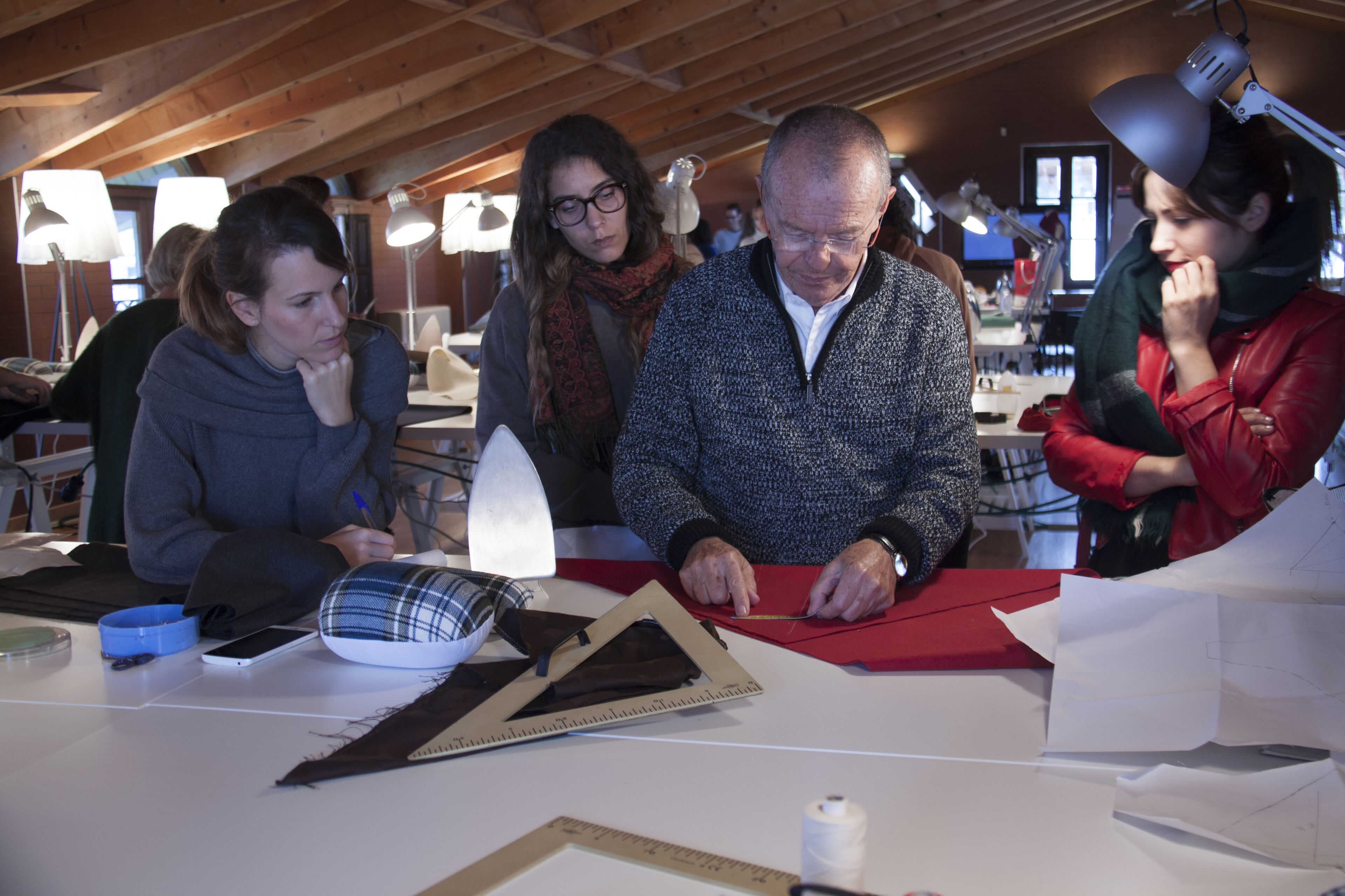 Un grupo de profesionales de la moda discuten atentamente y trabajan en la disposición de patrones sobre una gran mesa, en medio de un entorno de taller creativo.