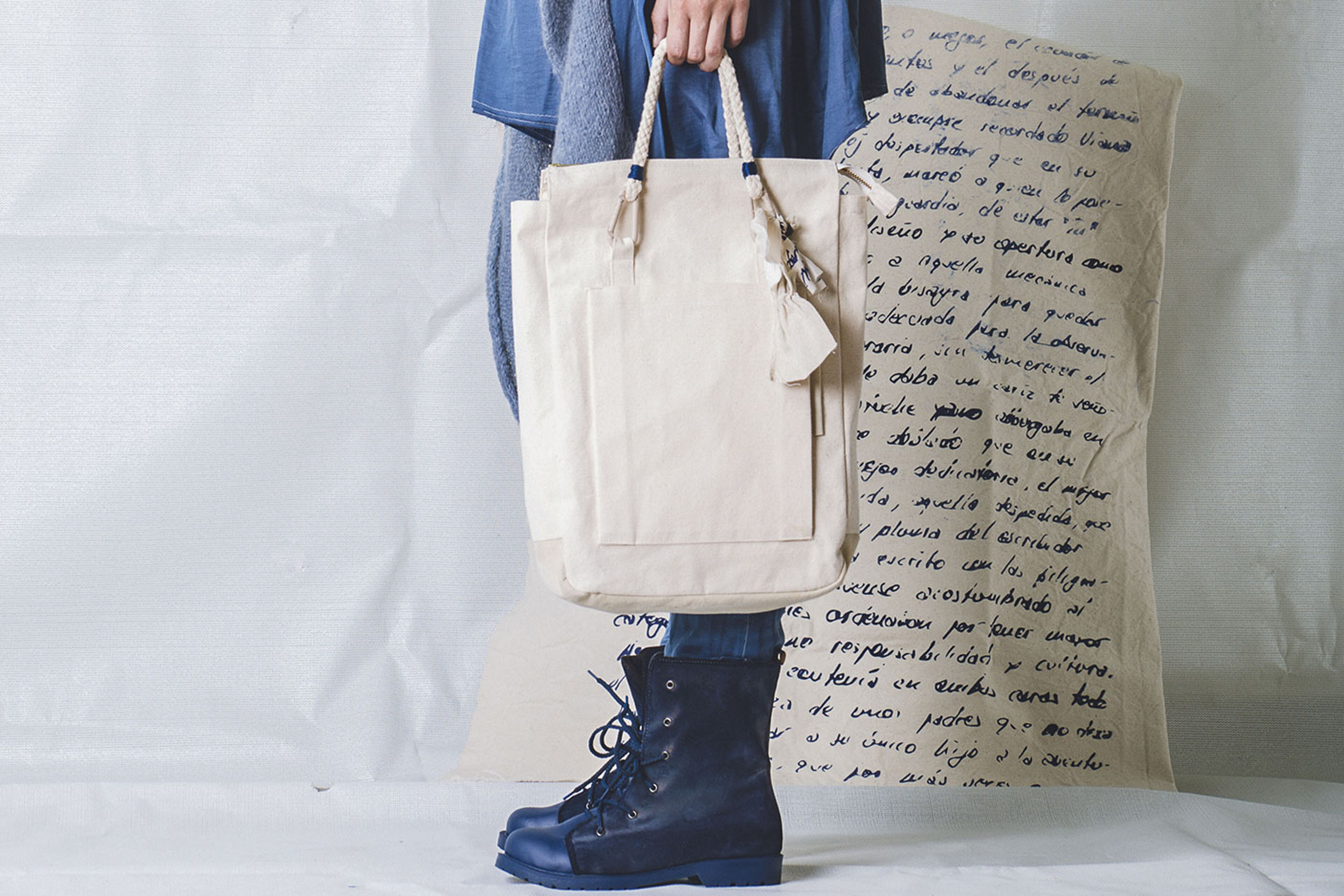 Una persona sosté una bossa tote de lona, mostrant un estil casual davant un fons de notes manuscrites.