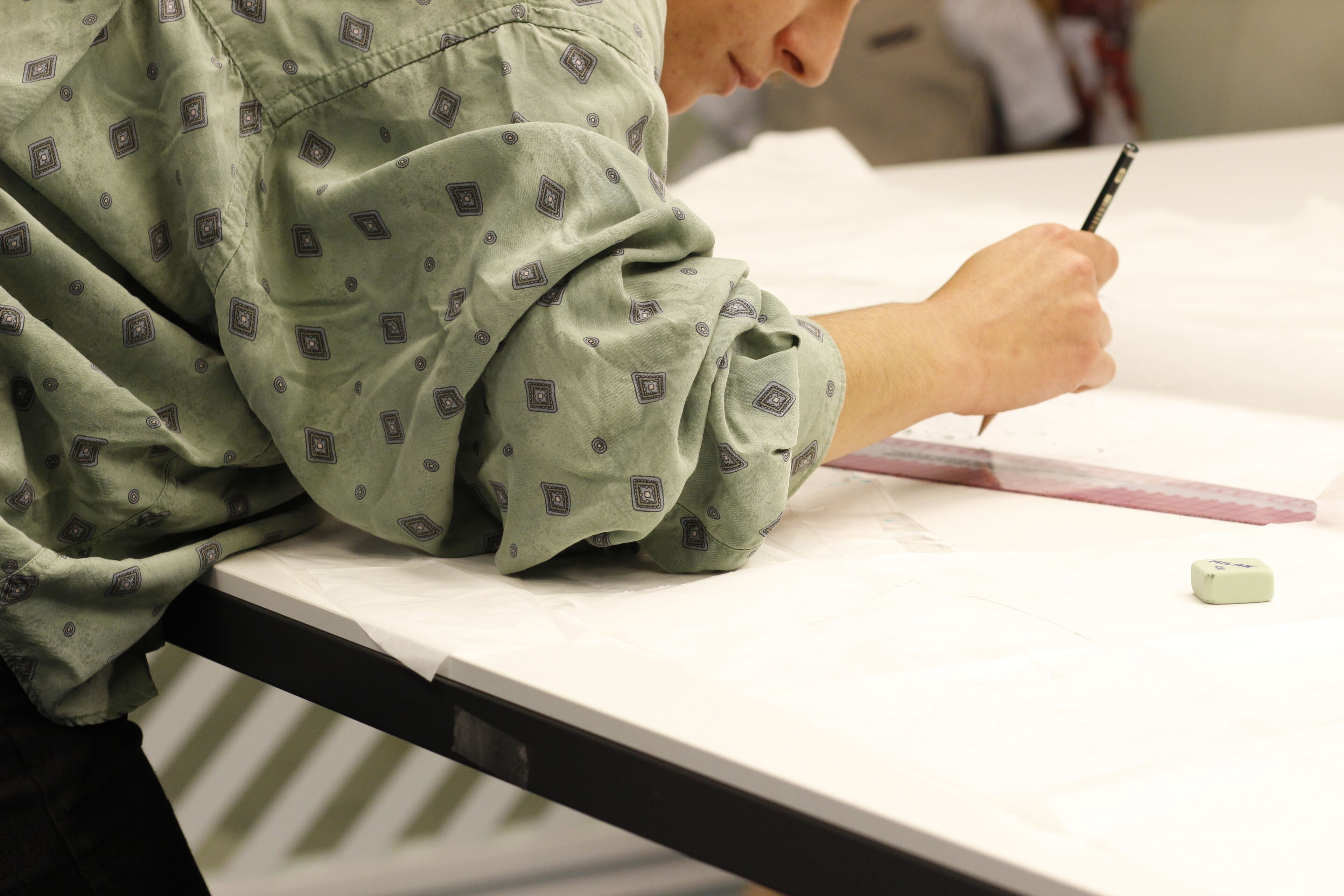 Un diseñador dibuja líneas precisas en papel de patrón, concentrándose intensamente en el proceso de trazado para confeccionar una prenda.