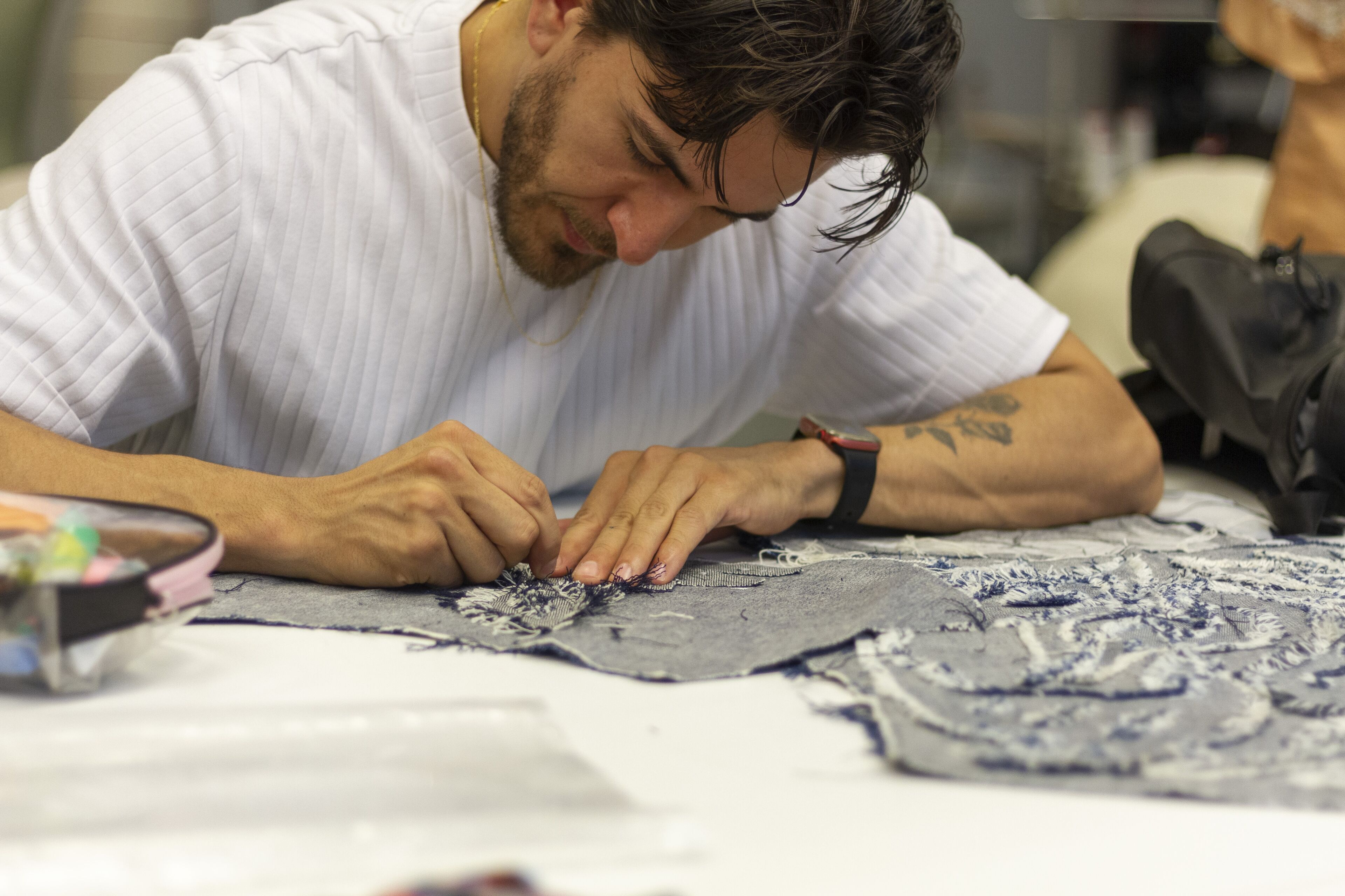 Un artesà meticulós broda amb cura un patró en un tros de teixit, concentrat en la feina delicada.