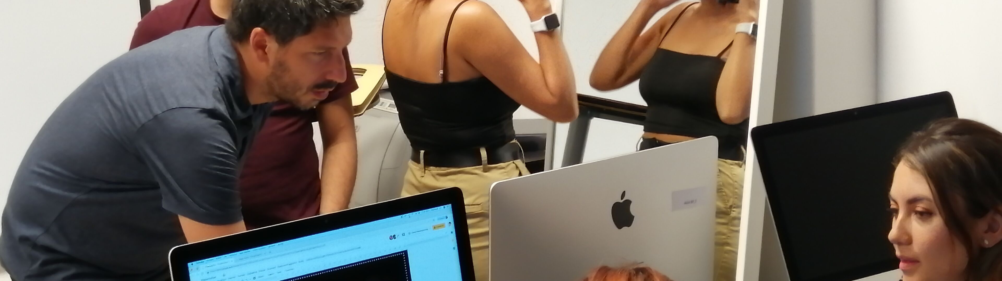 Un grup de professionals treballant junts al voltant d'ordinadors en una oficina, una persona ajustant un casc davant d'un mirall.