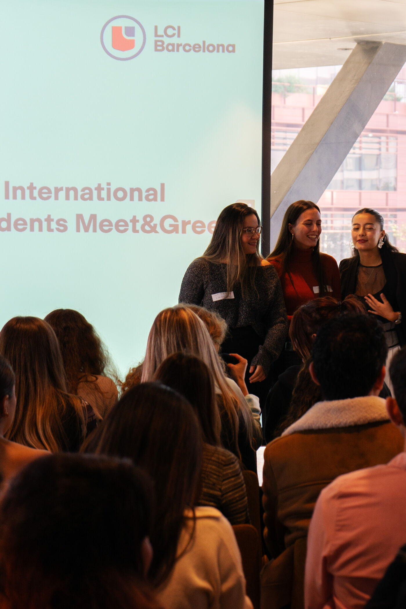 In the picture, there is a group of young people, possibly students, gathered in a room. They are sitting in chairs and listening to a speaker, who is giving a presentation or lecture. The room appears to be a classroom or a conference room, and the students are engaged in the discussion.