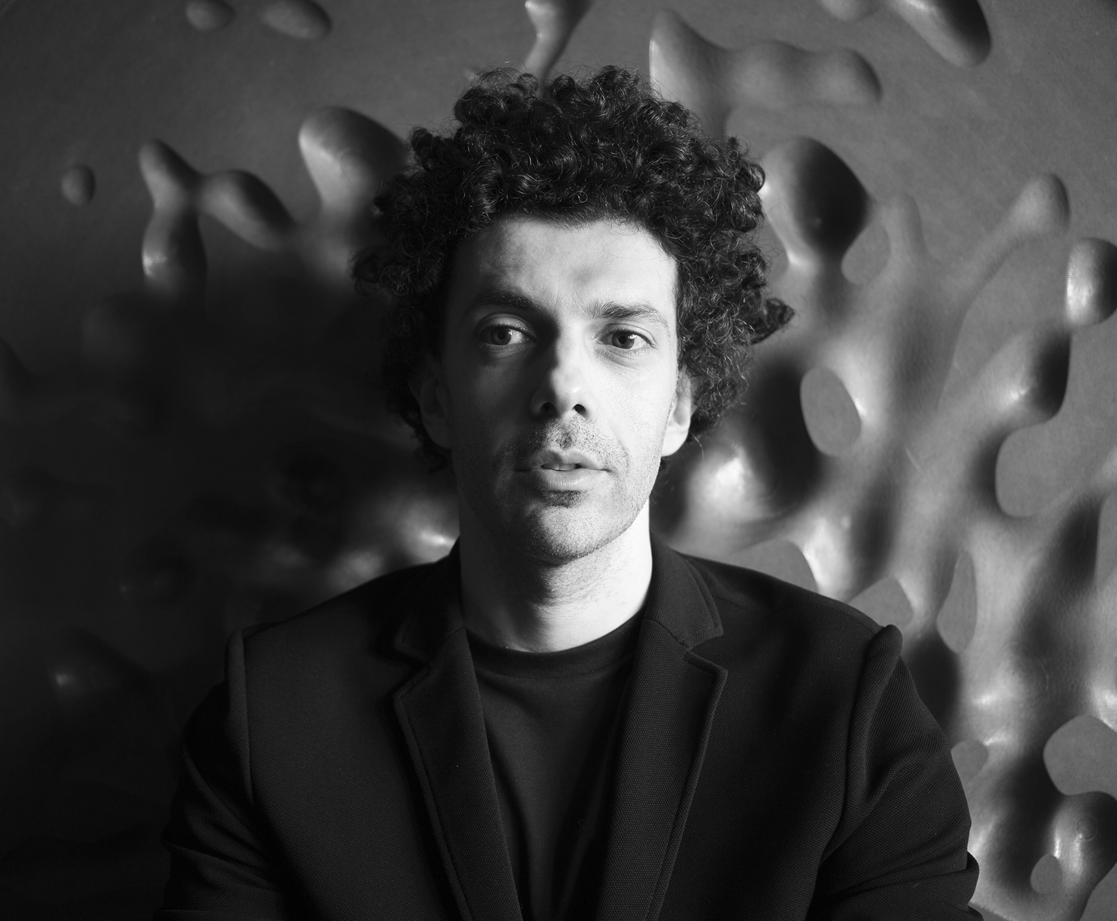 A monochrome portrait of a man with curly hair, gazing thoughtfully, set against a textured backdrop.