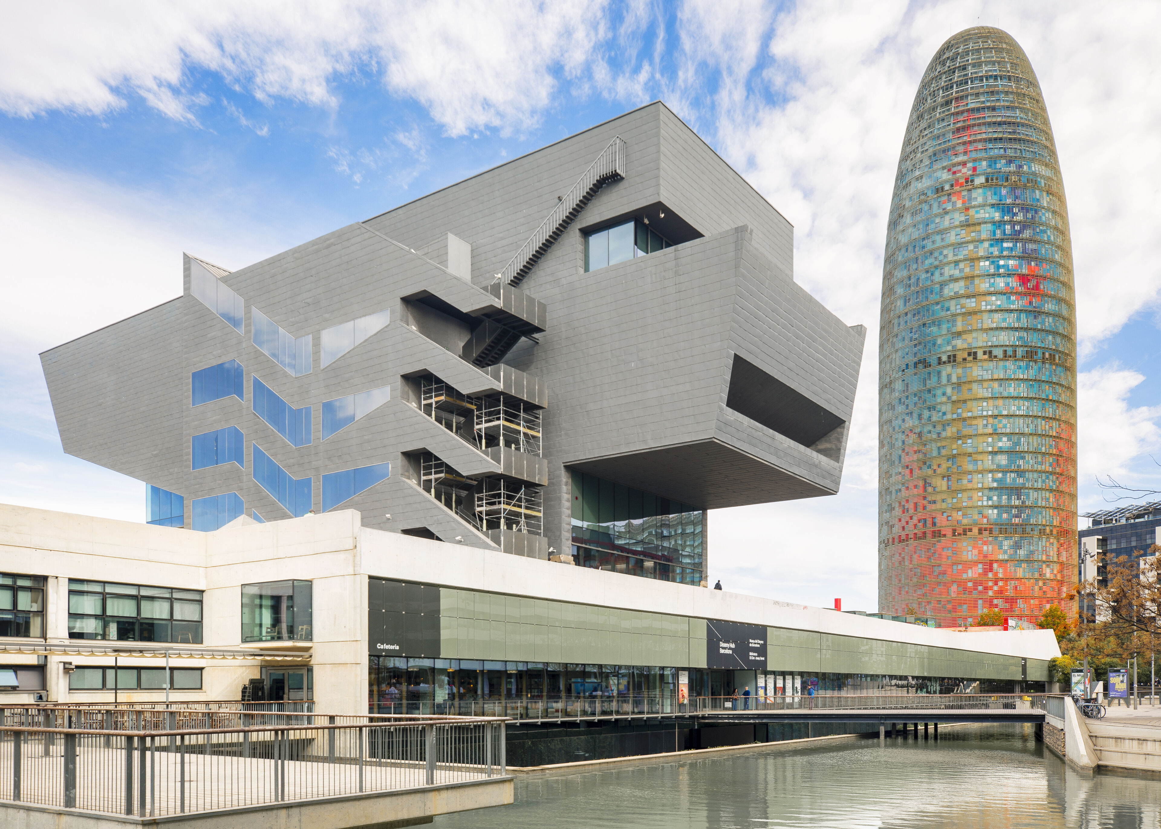 An avant-garde building in Barcelona juxtaposed with the colorful Torre Glòries, showcasing Spain's contemporary architectural landscape.