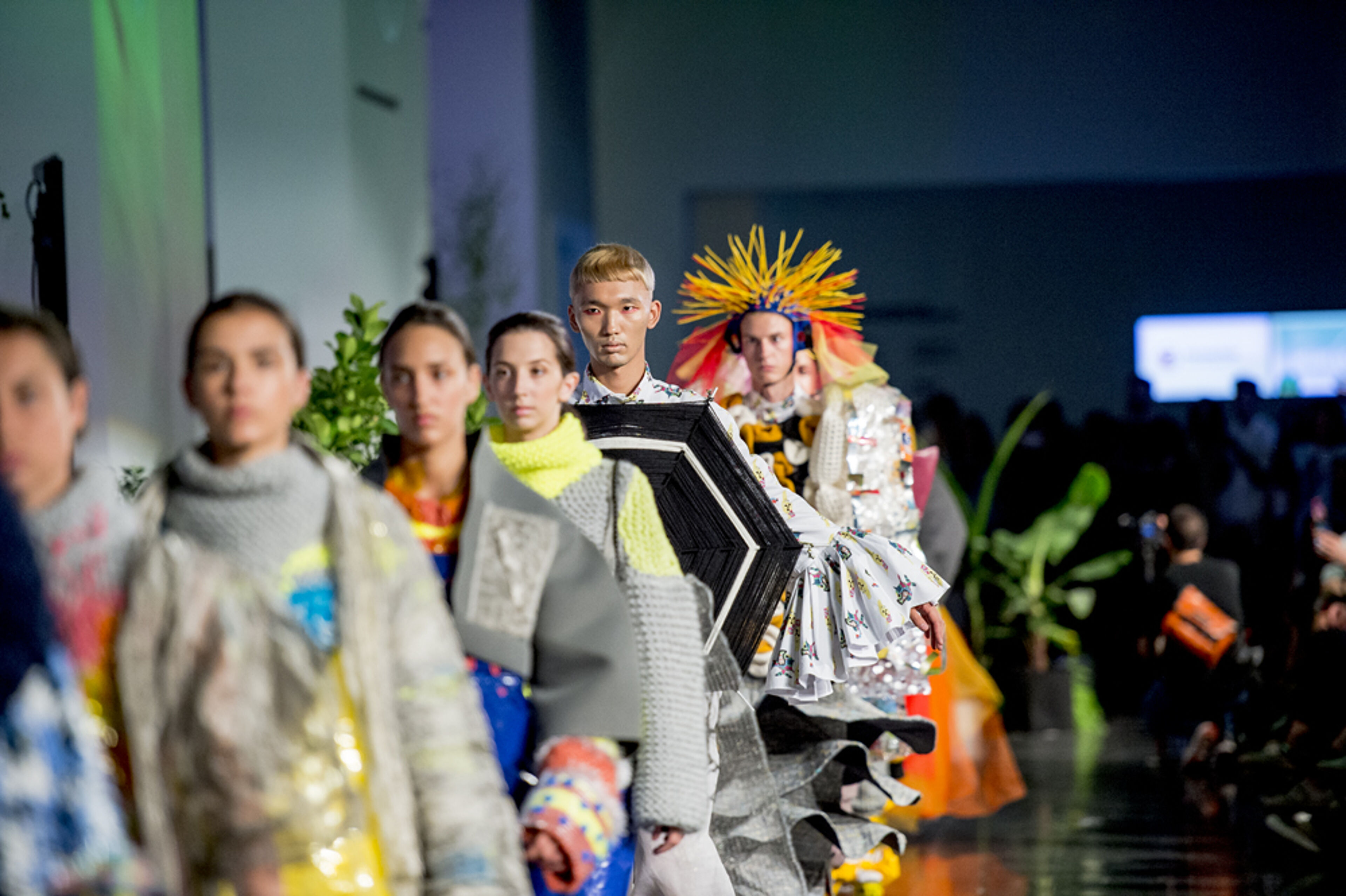 Models desfilen per la passarel·la amb vestits eclèctics i vibrants en un esdeveniment de moda contemporani, mostrant un disseny innovador i textures atrevides.