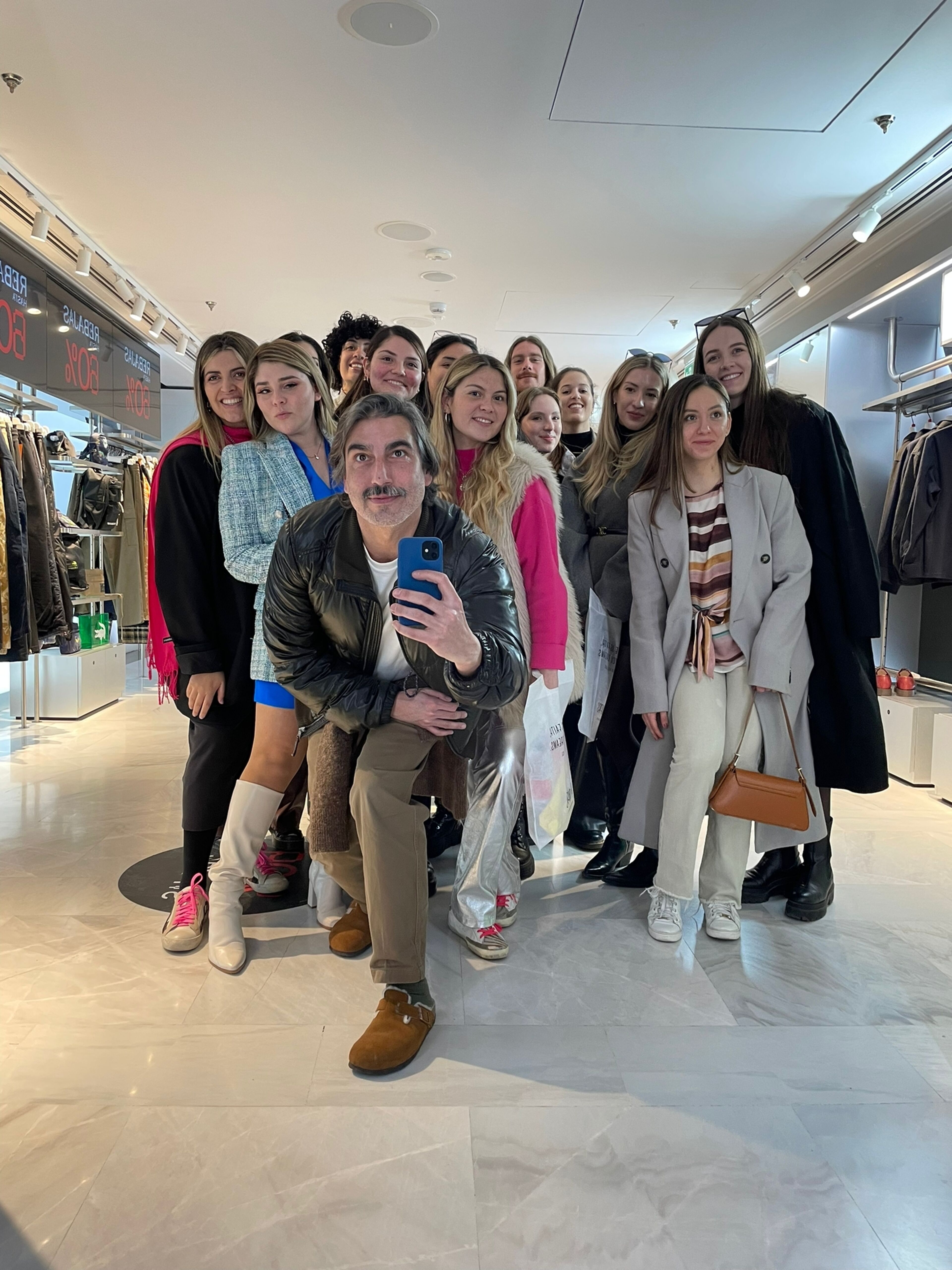 A cheerful group of people posing for a mirror selfie in a clothing store, with a man in the forefront holding the phone.