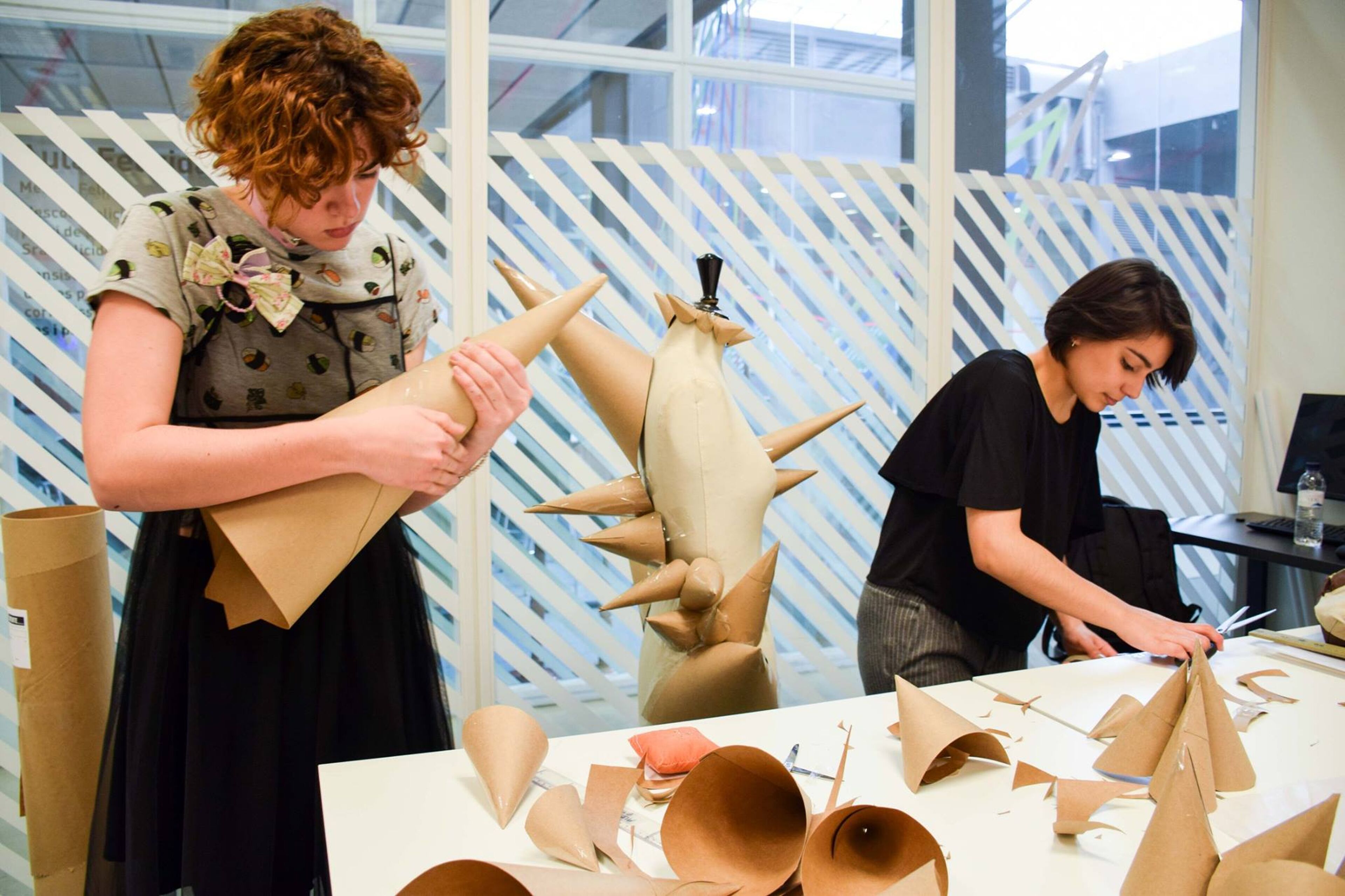 Two art students are engaged in creating sculptures from cardboard, focusing intently on their work.