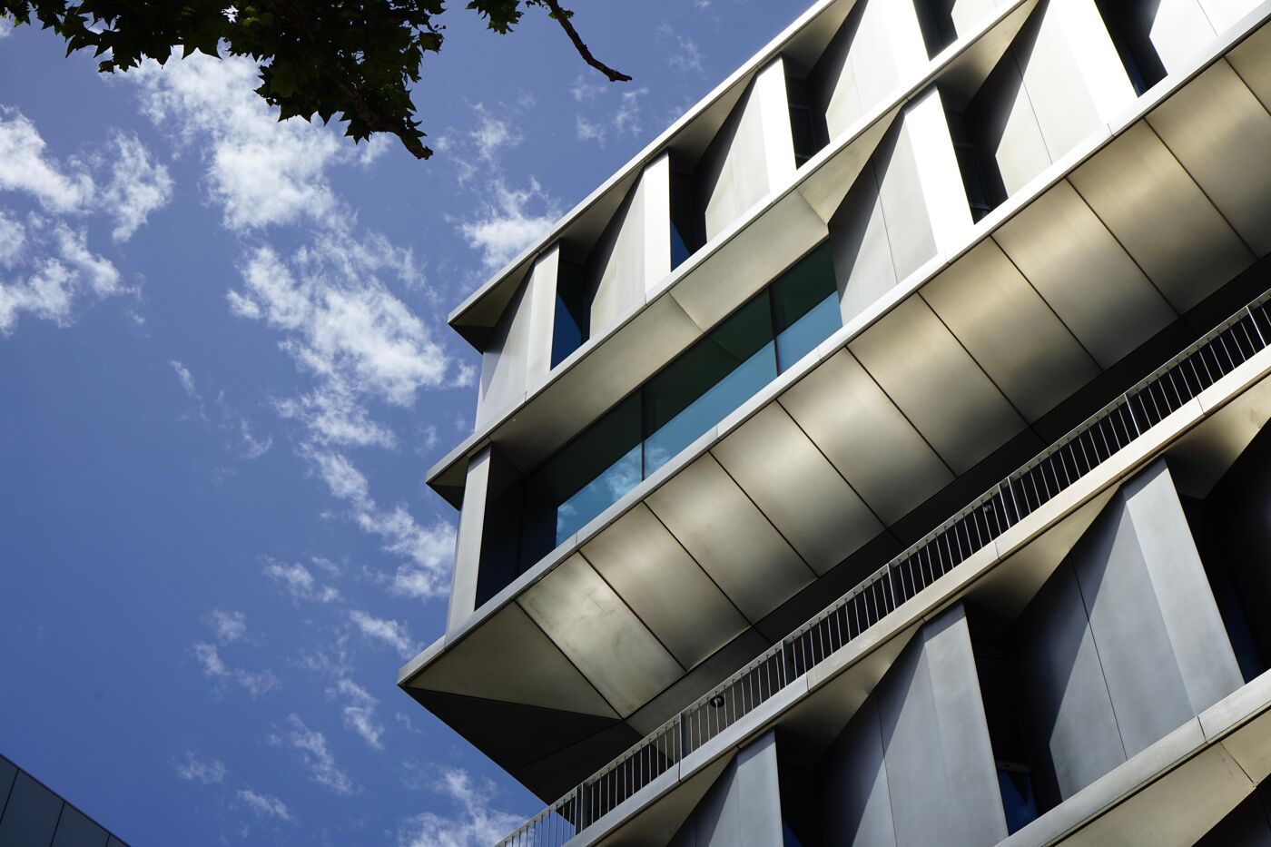 Low-angle view of a modern building with a metallic facade and geometric design against a partly cloudy sky.