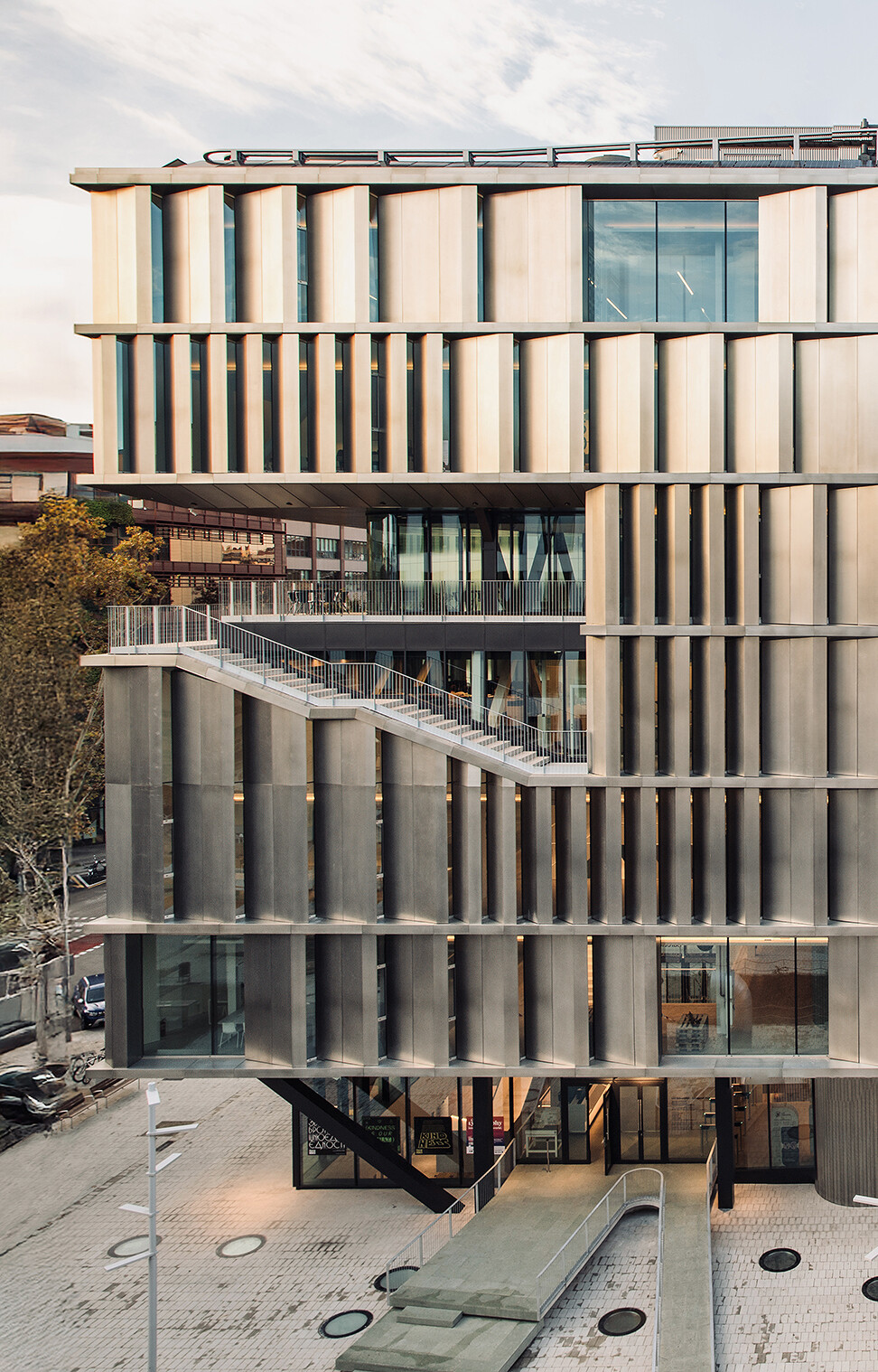 Eye-level view of a modern building with a distinctive facade of vertically-oriented, textured metallic panels, featuring a prominent staircase and large windows.