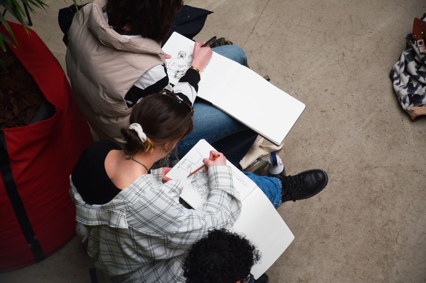 High-angle view of two people sitting on the floor, sketching on large sheets of paper.