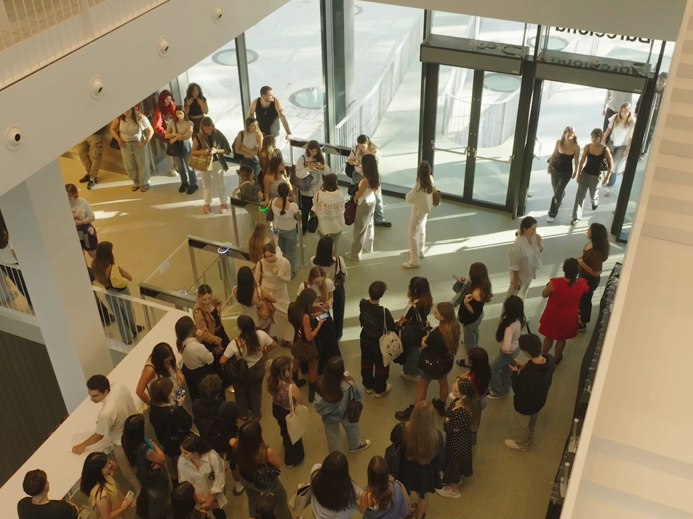 High-angle view of a large group of young people congregating in a modern, multi-level building with glass walls and a high ceiling.