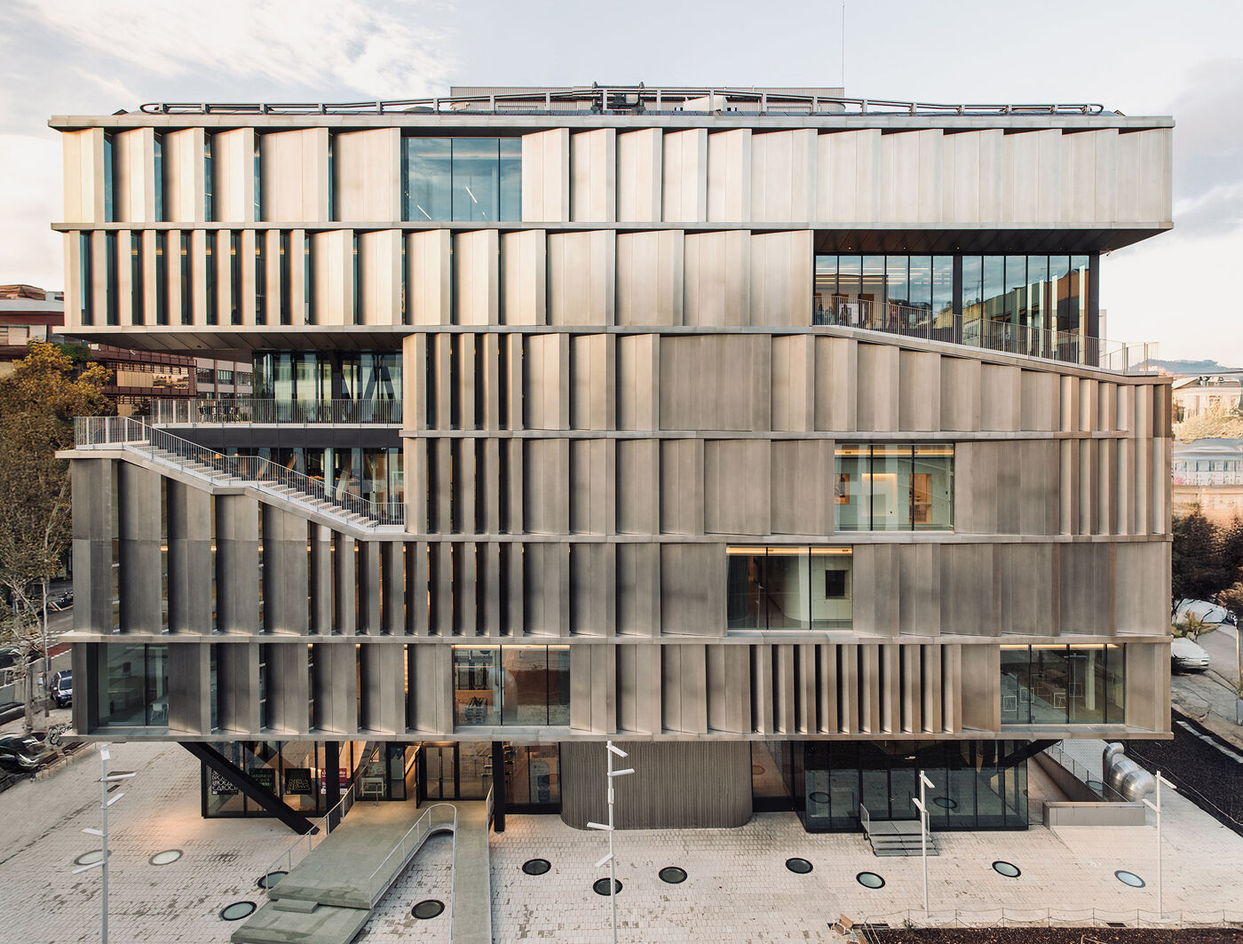 Eye-level view of a modern building with a distinctive facade of vertically-oriented, textured metallic panels, featuring a prominent staircase and large windows.