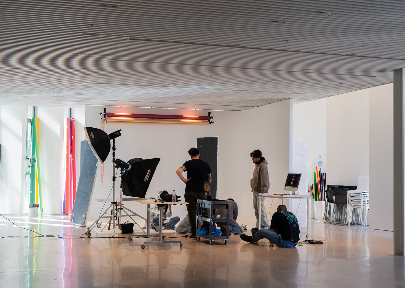 A photography studio with several people working on a photoshoot, surrounded by lighting equipment, backdrops, and props.