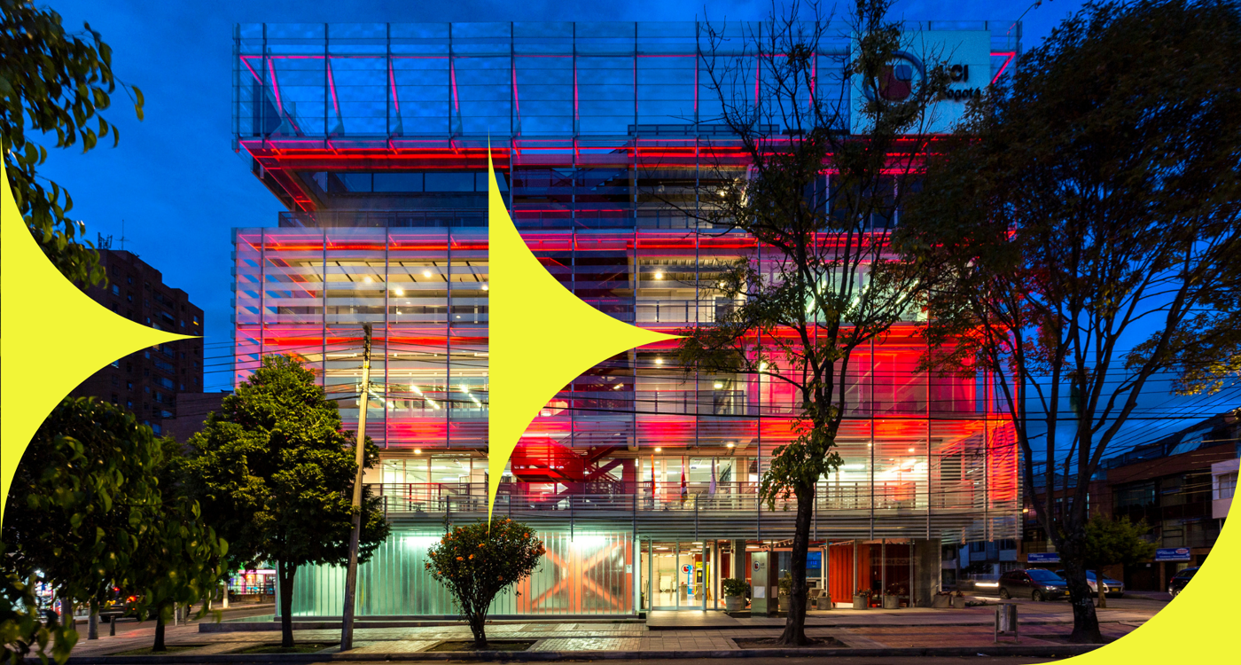 A modern building with glass facades and bright red interior lighting, surrounded by trees under a twilight sky.
