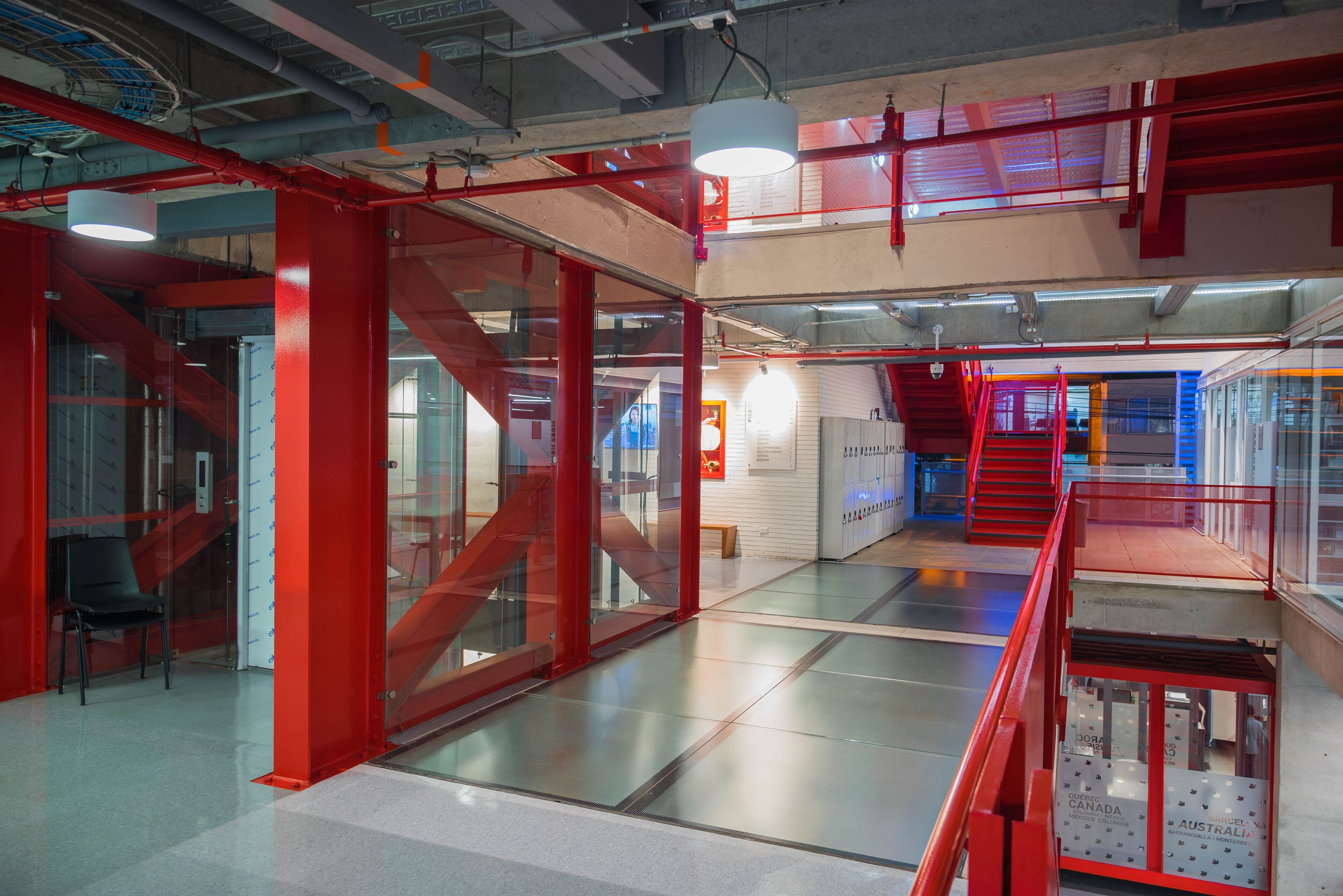 Interior view of an office with industrial design elements, featuring red structural beams, glass partitions, and modern lighting.