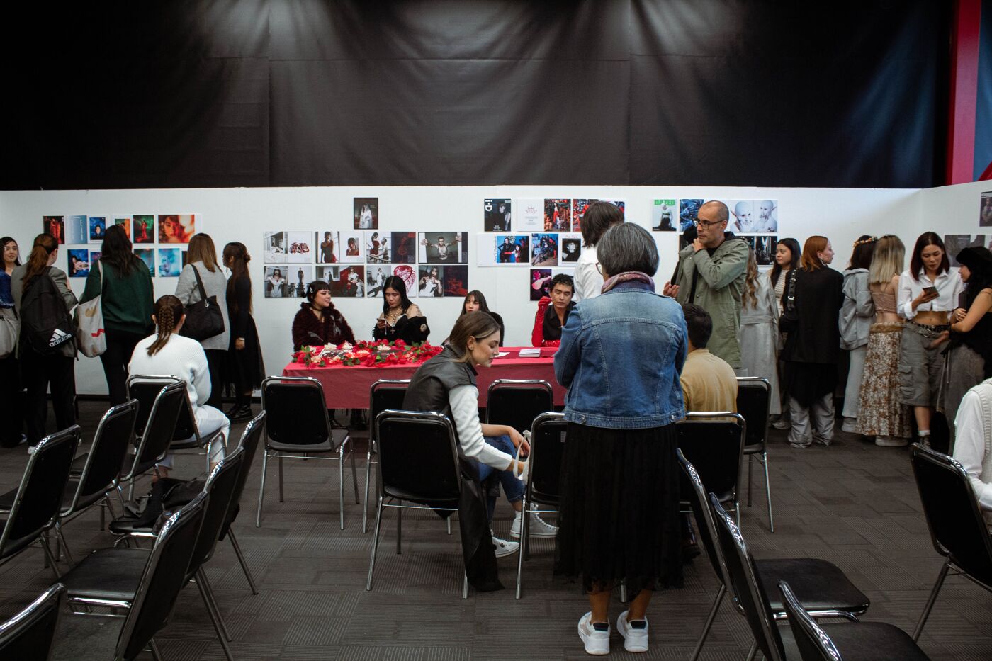 Attendees at the opening of an art exhibition, observing artworks displayed on panels, with a registration table adorned with flowers.