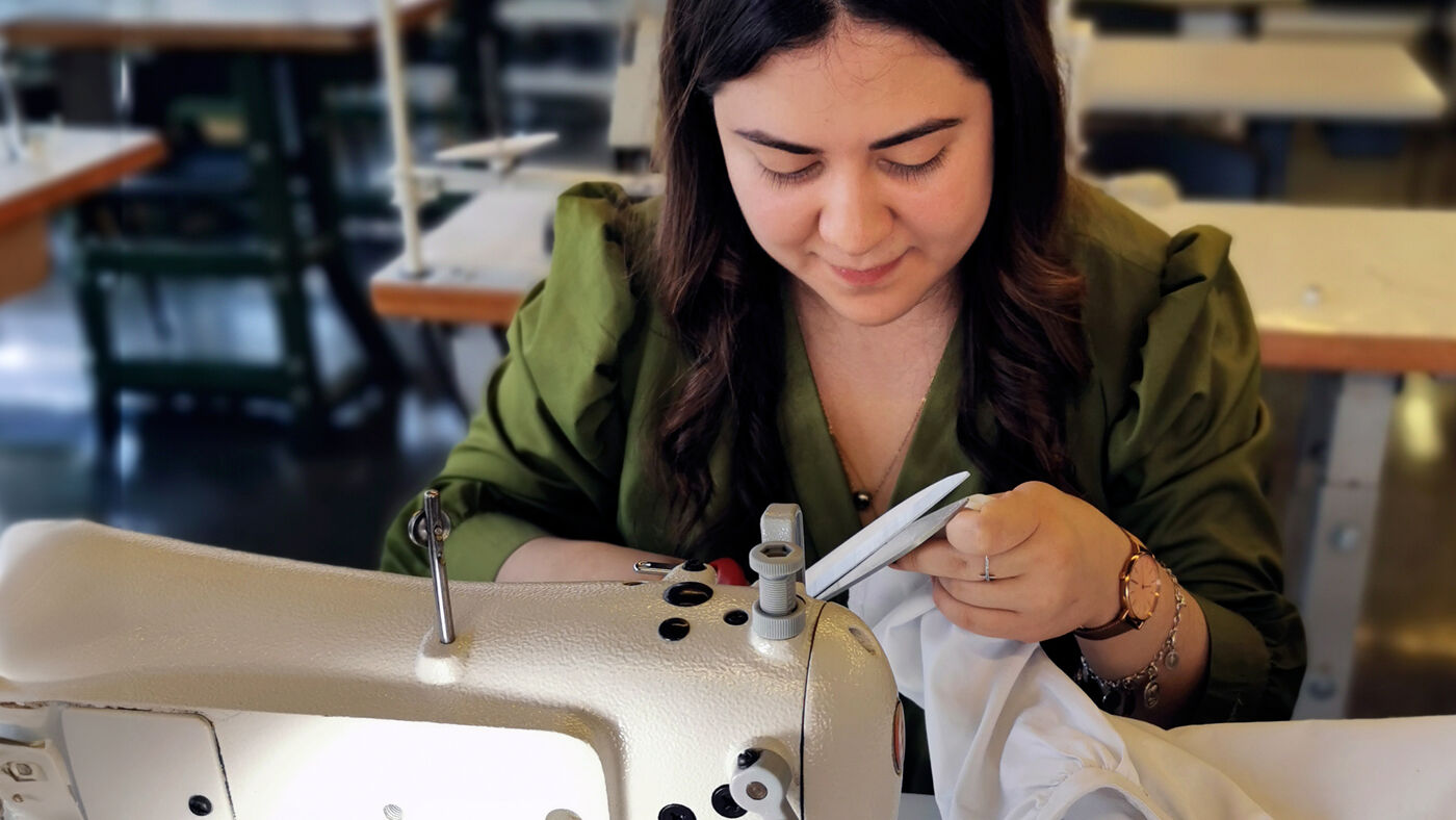  A focused fashion student working with a sewing machine in a textile class, surrounded by empty workstations.

