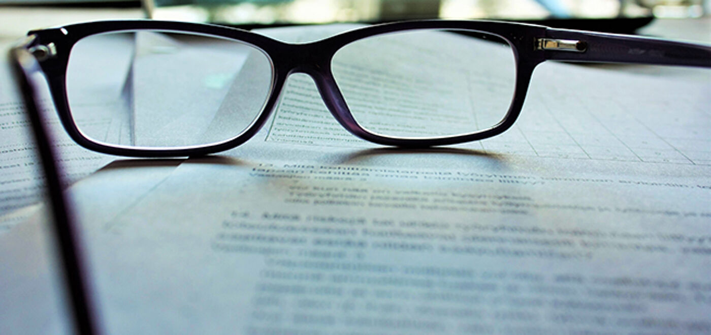 A pair of black-framed eyeglasses resting on a sheet of printed text.