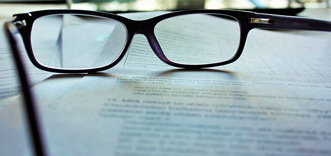 Un par de gafas con montura negra descansando sobre una hoja de texto impreso.