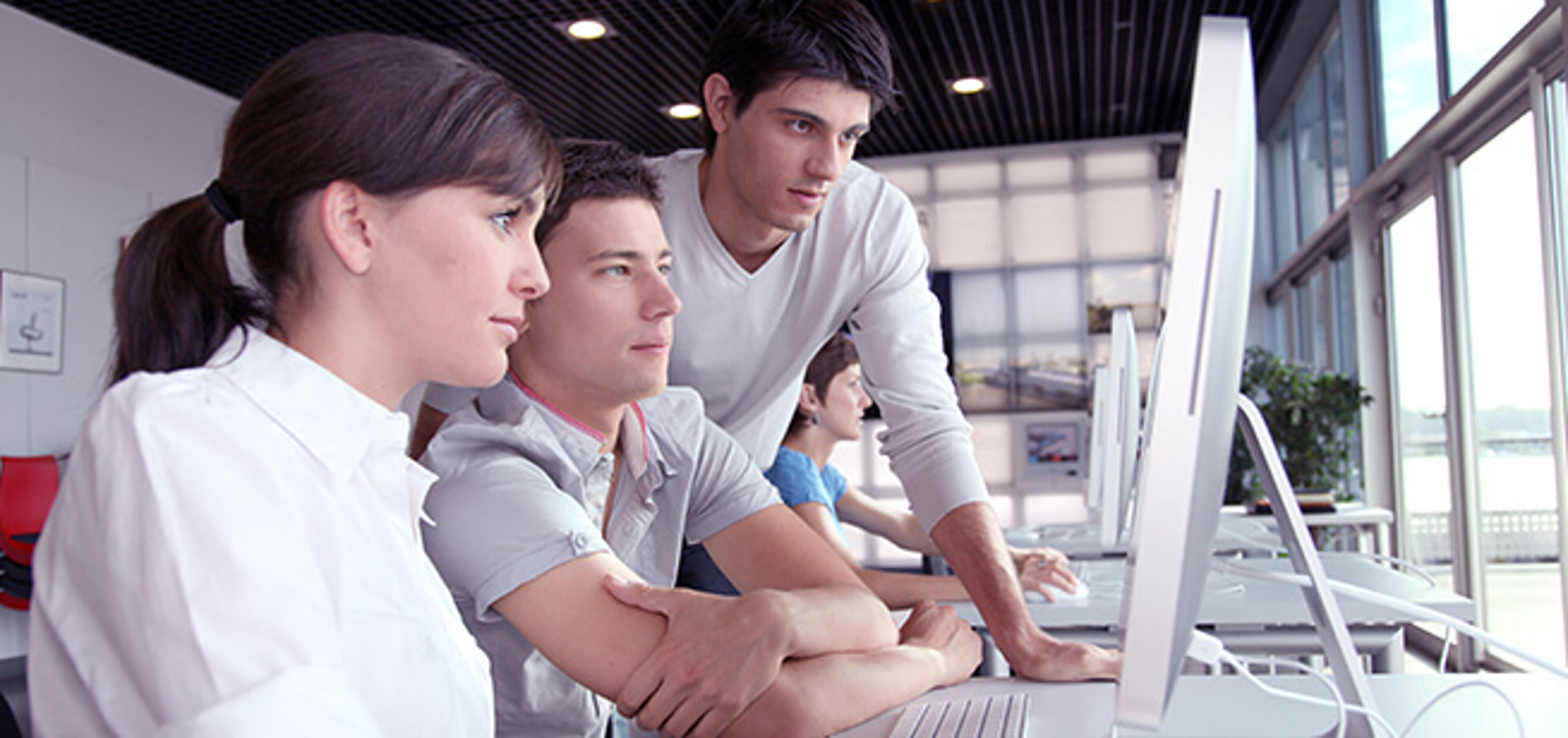 Three professionals collaboratively working at computer stations in a bright office environment.