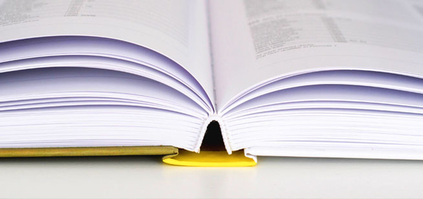 A hardcover book with white pages lies open on a table, its spine resting on the yellow book cover.