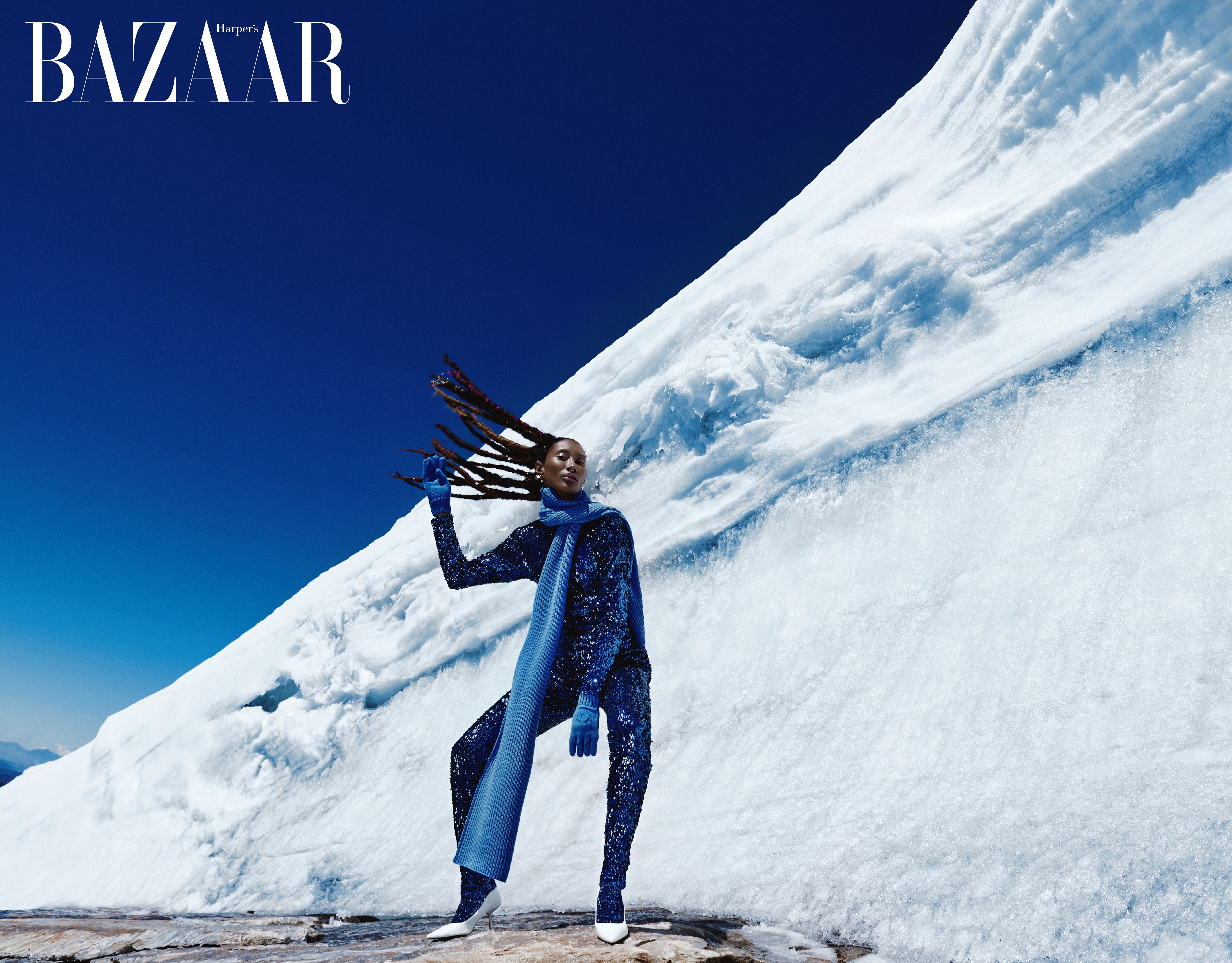 Modelo posa en conjunto azul elegante contra un impactante fondo de hielo para Harper's BAZAAR.