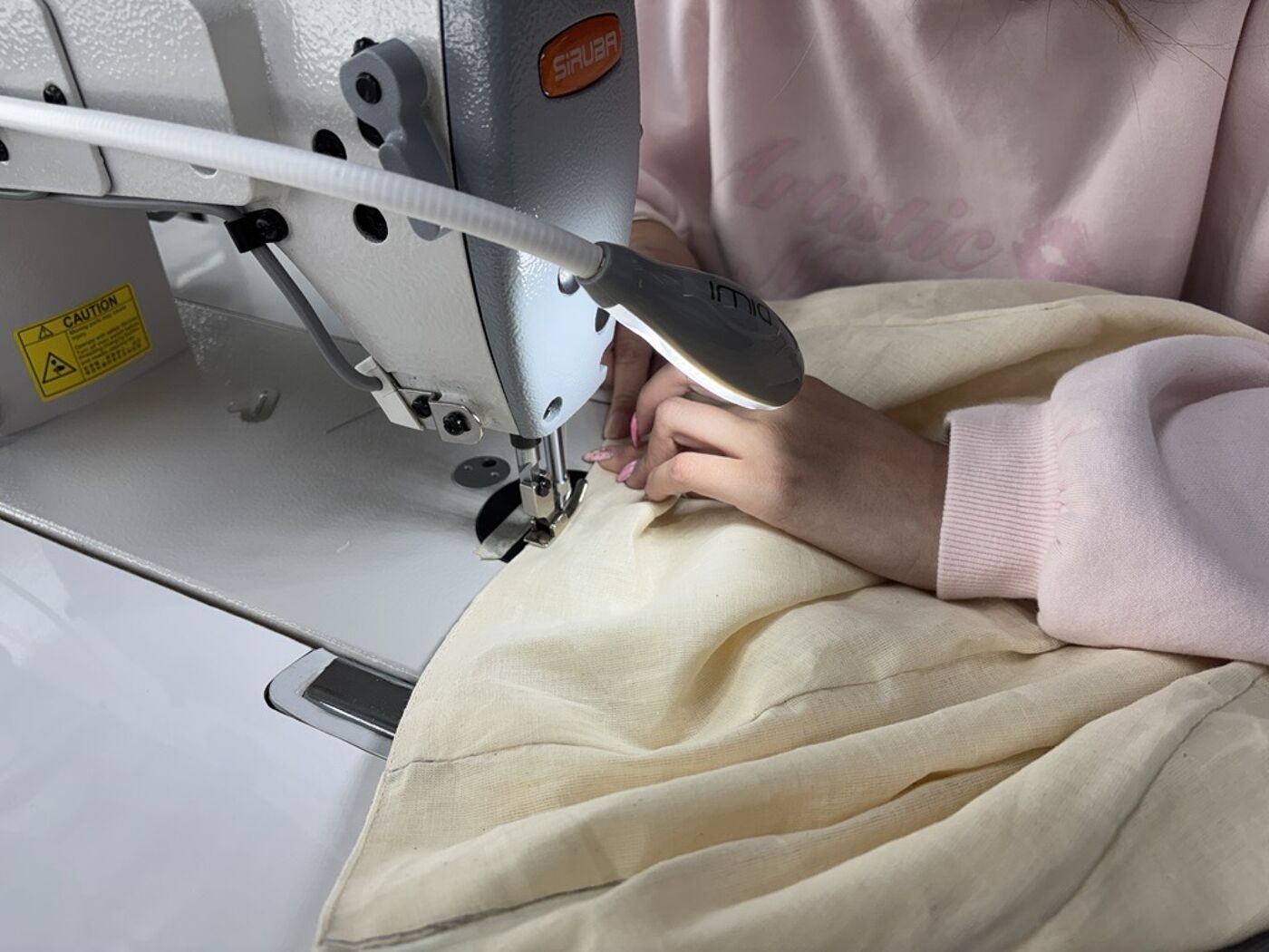 A person is using a sewing machine to stitch fabric, with a bright LED light illuminating the work area for precision.