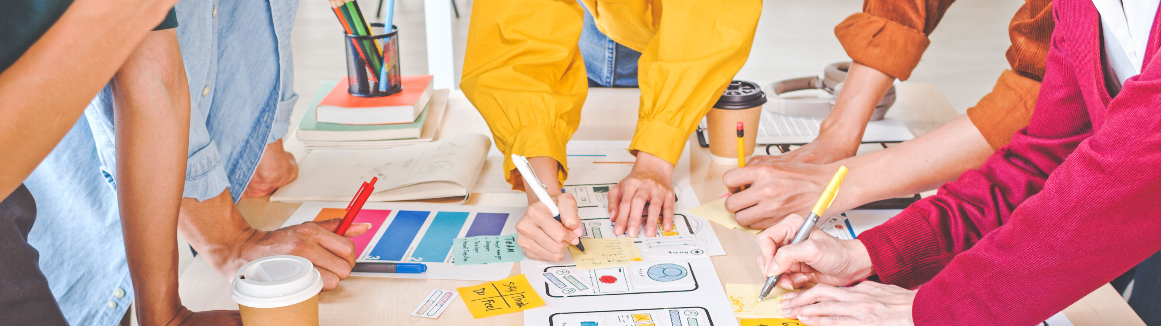 Un equipo de profesionales participa en un taller creativo, trabajando en maquetas de diseño y notas de colores esparcidas en una mesa.