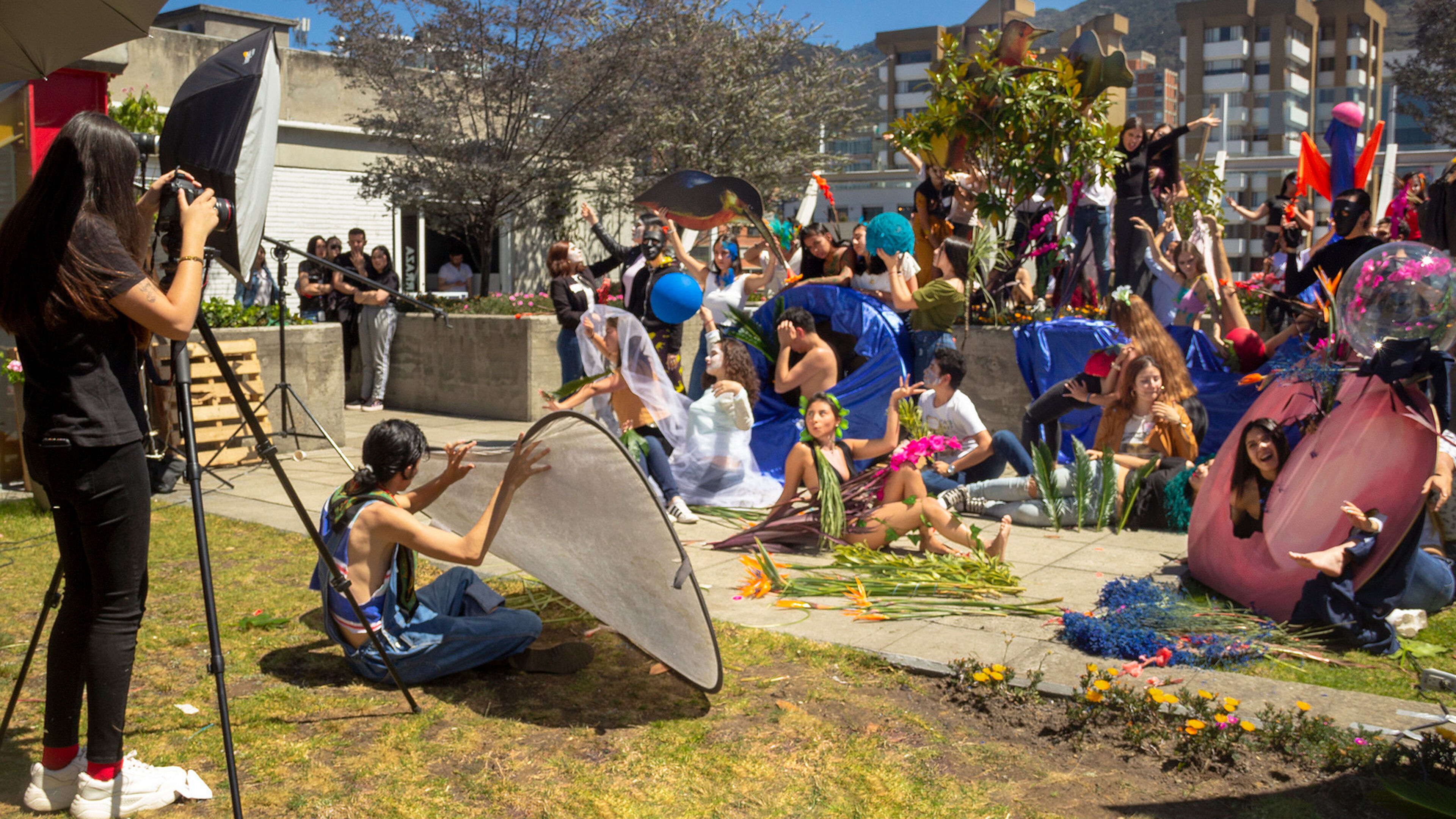 A dynamic outdoor photoshoot with performers in colorful costumes simulating a theatrical scene, surrounded by onlookers and photography equipment.