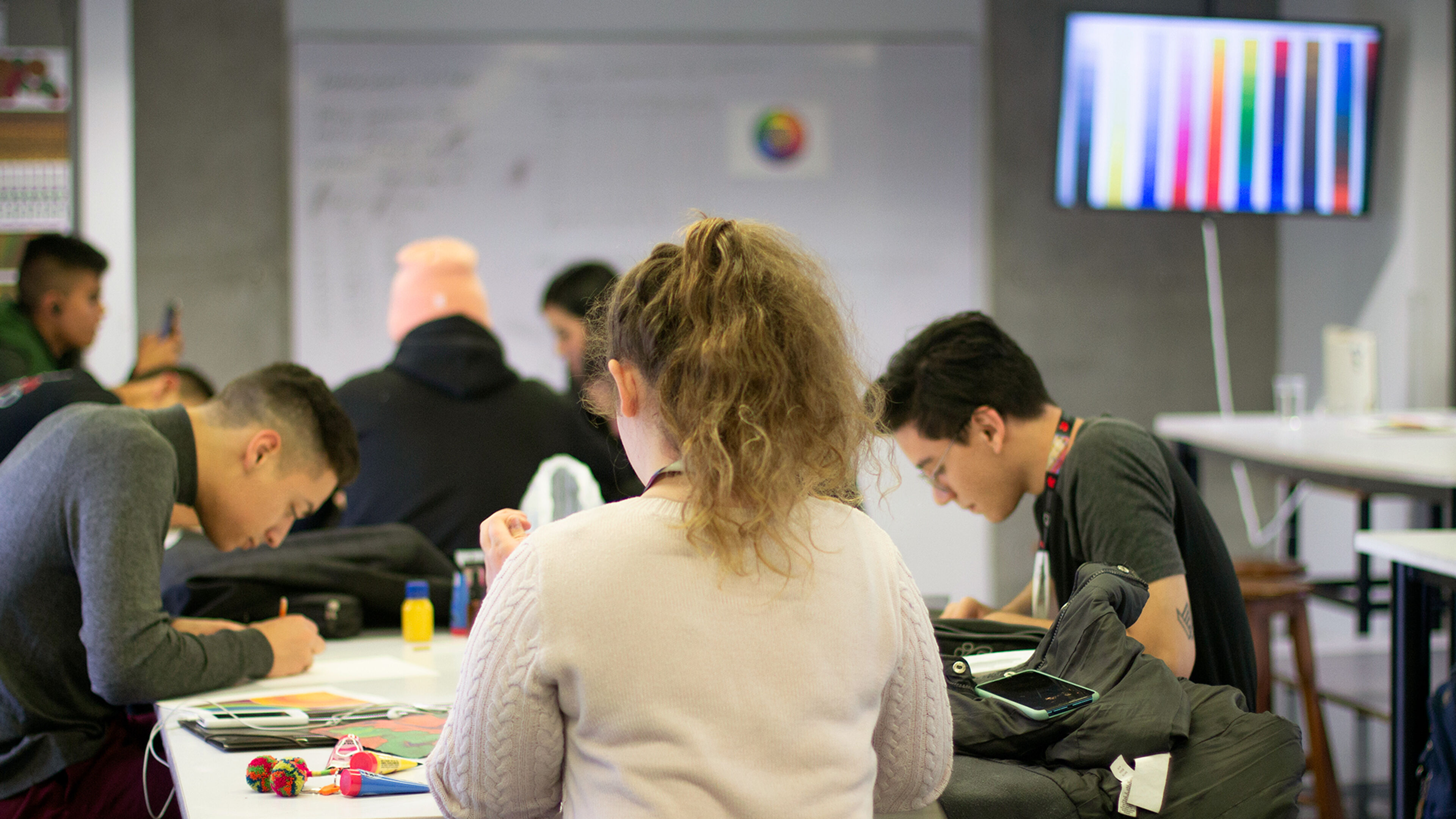 Students focused on their work in a well-lit classroom, with colorful digital art displayed in the background, creating a vibrant learning environment.