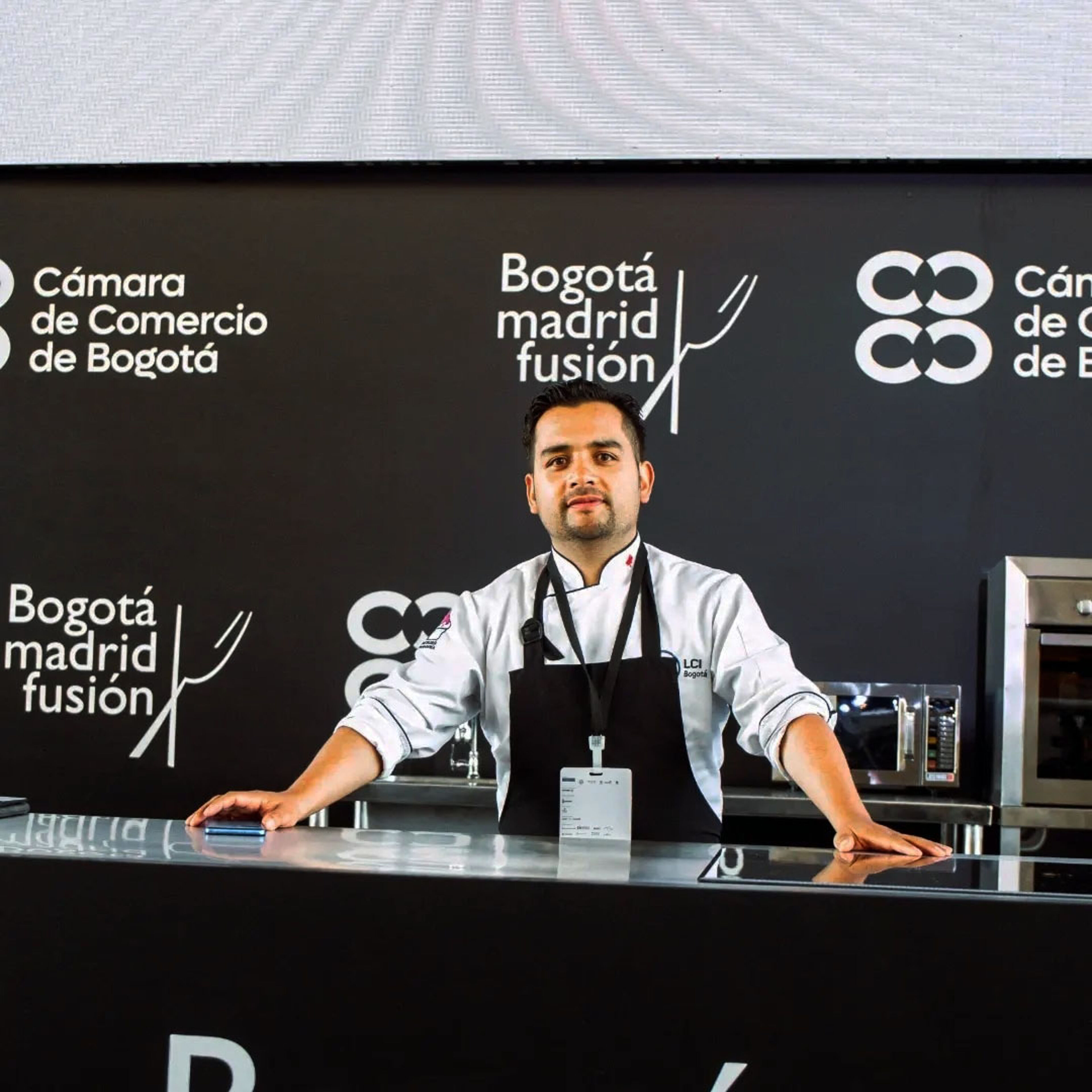Un chef confiado en atuendo profesional está detrás de un mostrador de presentación en el evento 'Bogotá Madrid Fusión'.