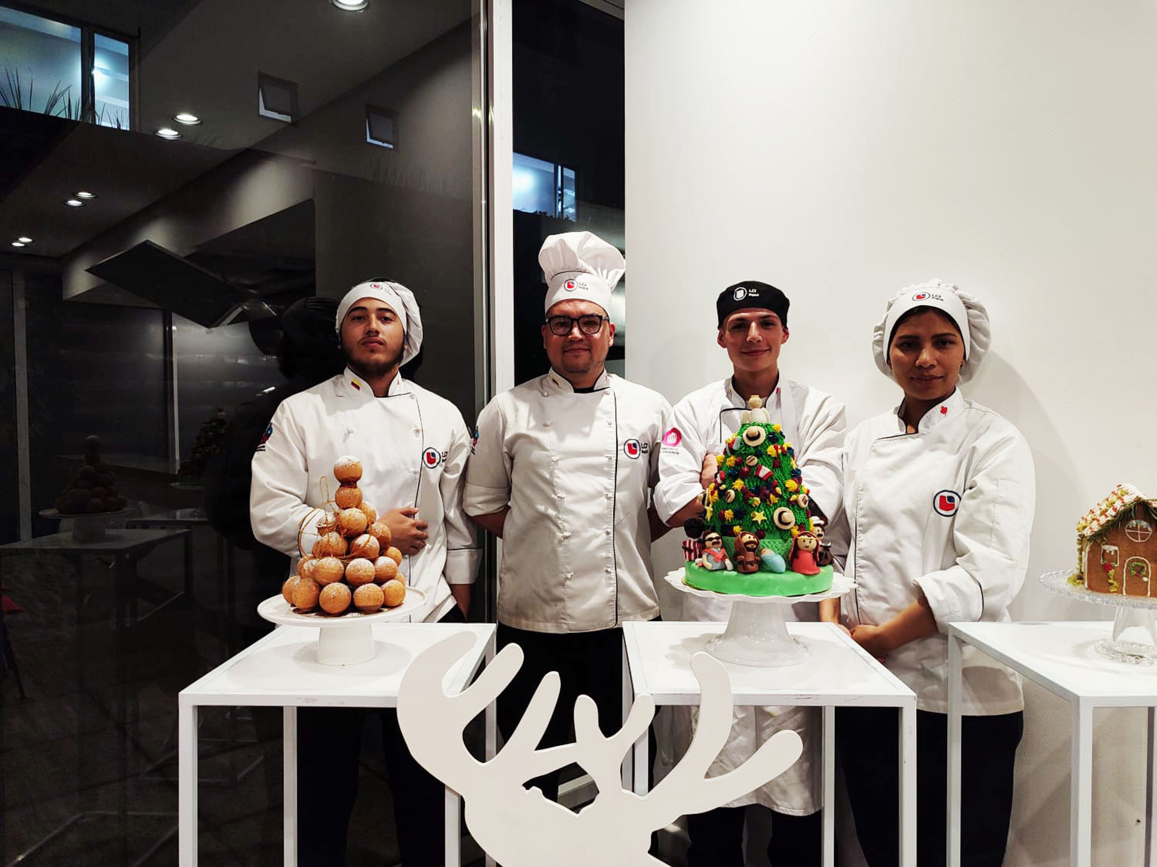 Cuatro pasteleros uniformados mostrando sus creaciones festivas, incluyendo un croquembouche, un pastel de árbol de Navidad y una casa de jengibre.