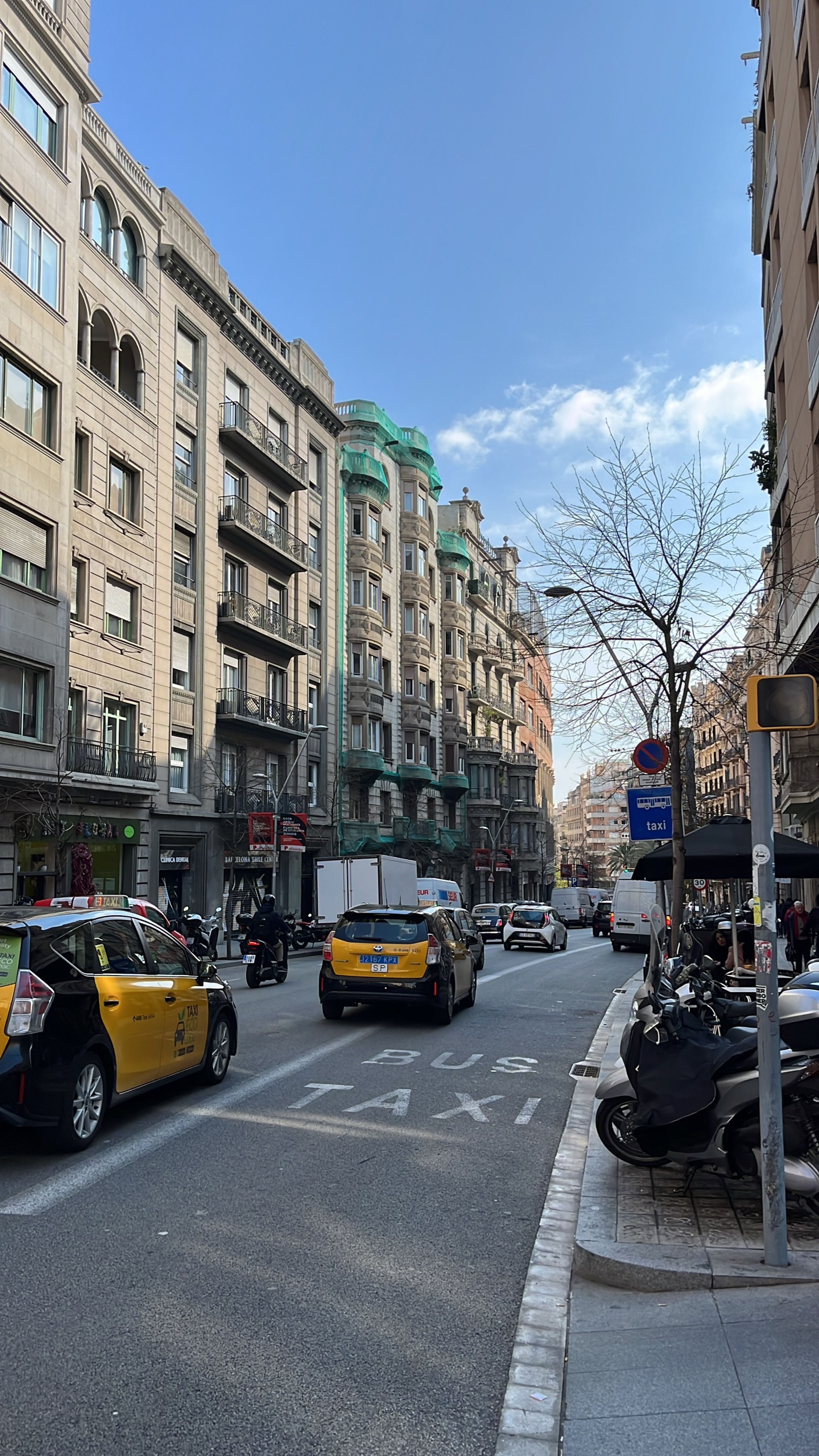 Una calle de la ciudad con edificios de estilo europeo con cúpulas verdes, tráfico activo con taxis amarillos distintivos y un cielo azul brillante encima.