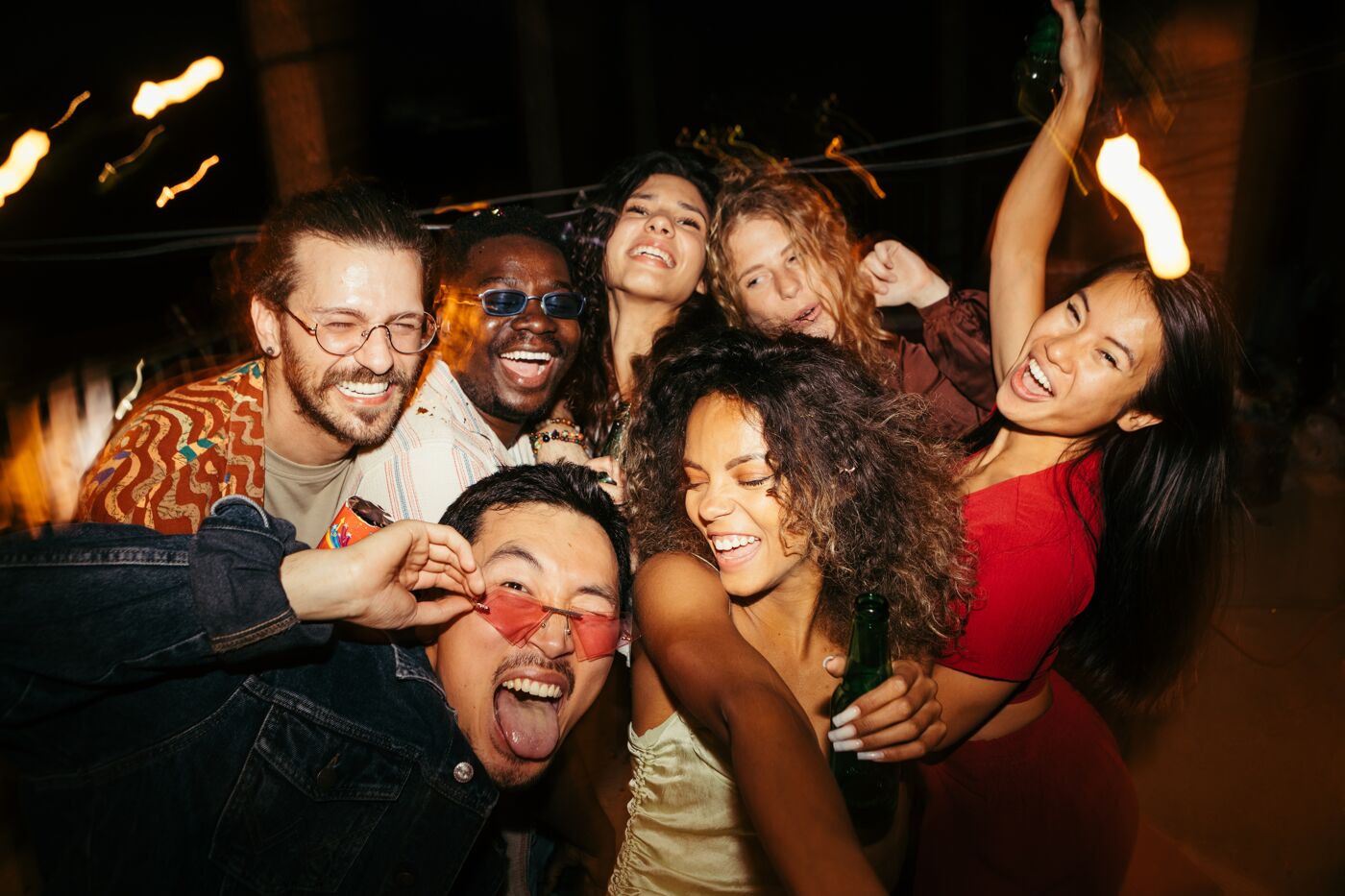 A diverse group of six friends laughing and enjoying a festive evening together, captured in a moment of genuine happiness.